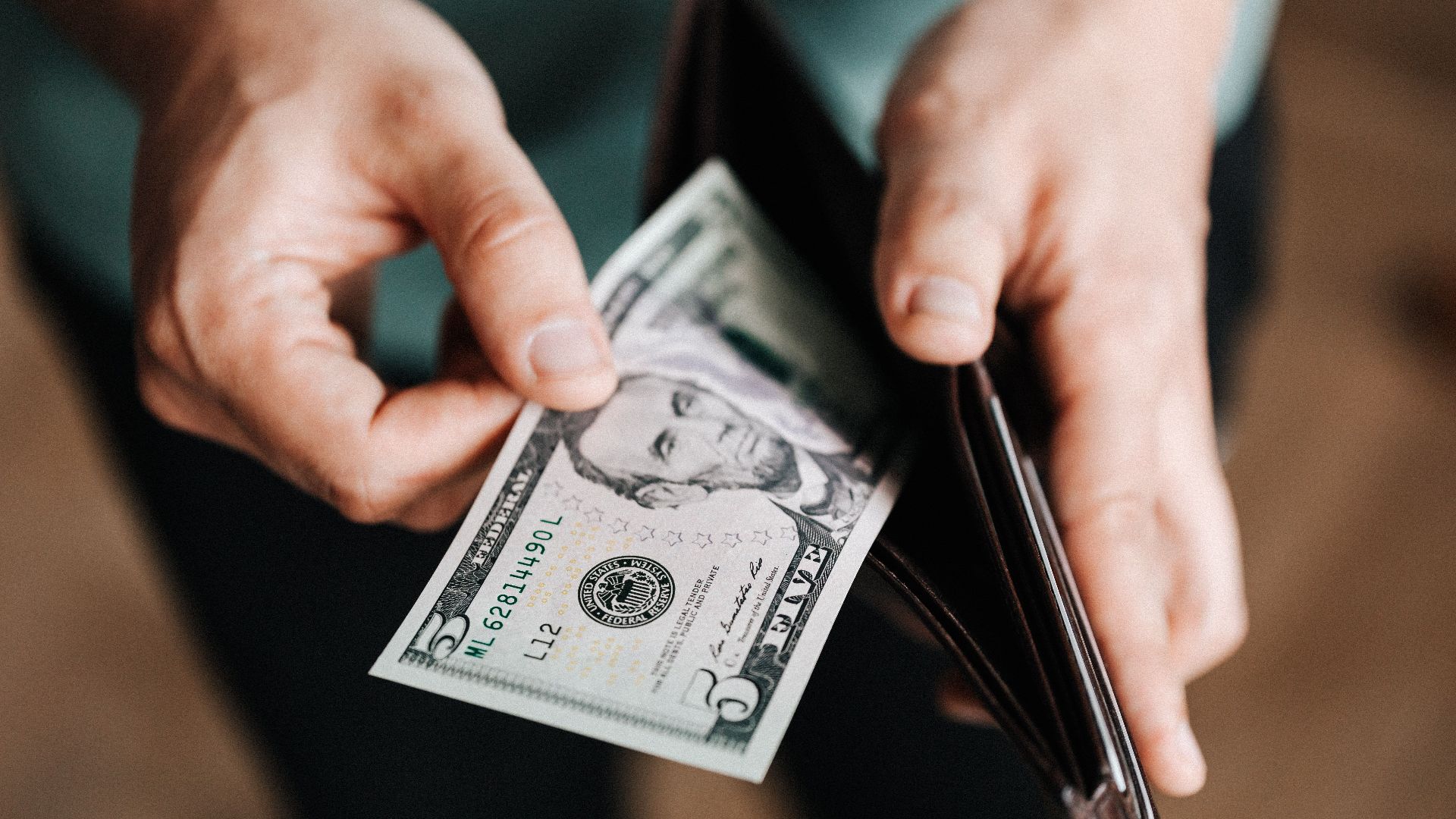 Closeup of crop male in casual clothes taking dollars out of wallet while paying in shop