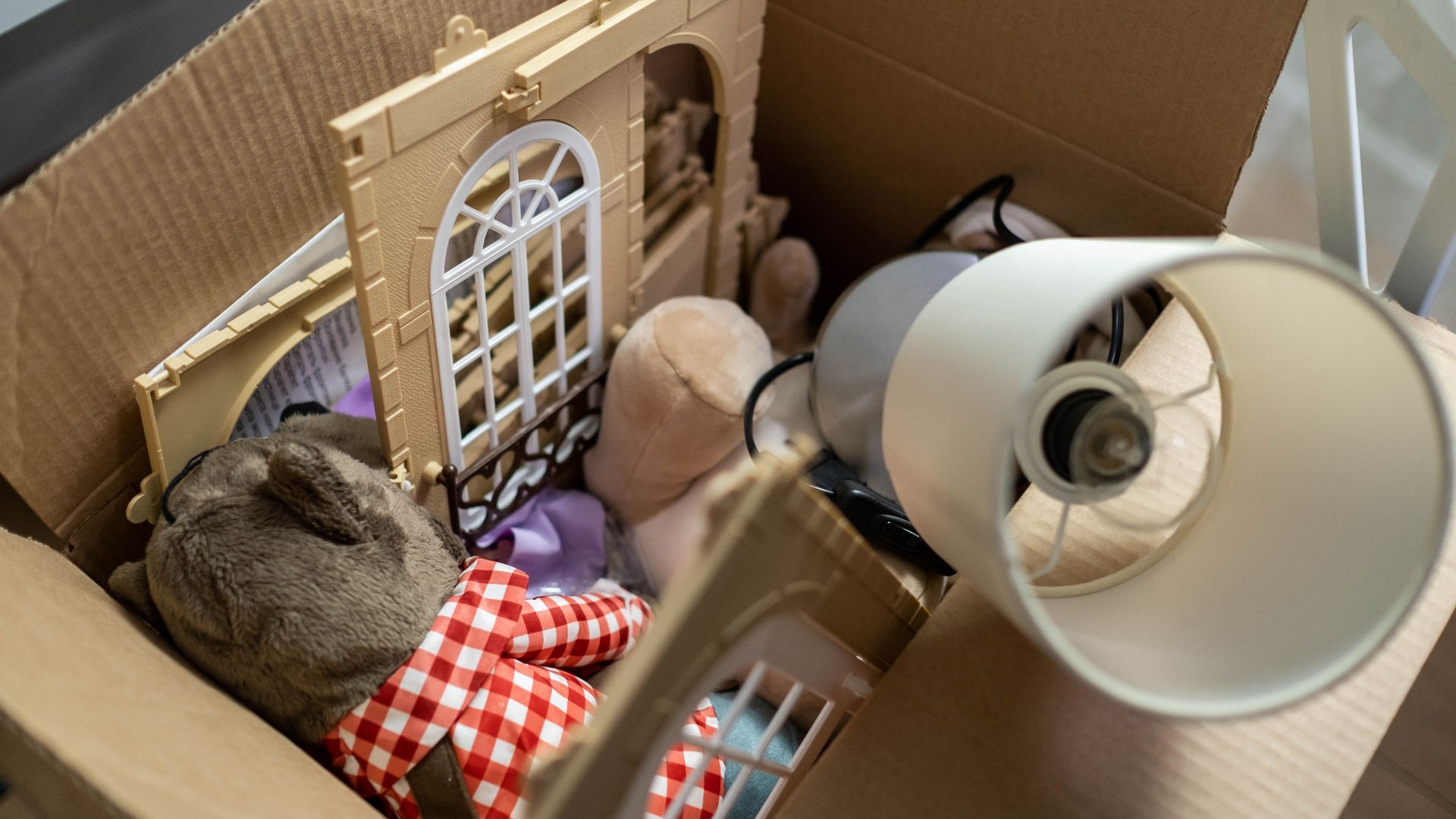 Cardboard box containing toys and a lampshade, perfect for moving or storage themes.