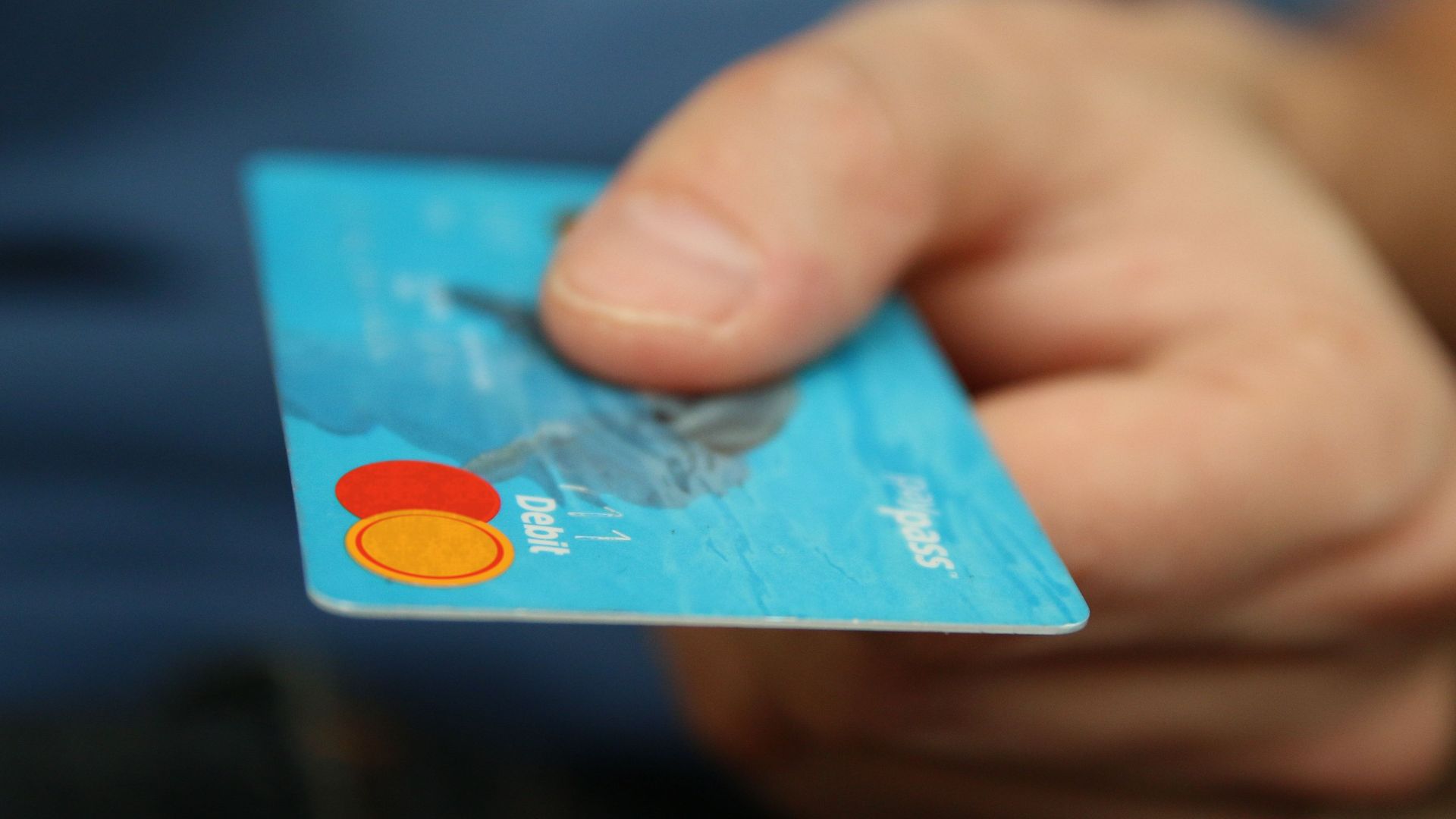 A close-up shot of a hand offering a blue debit card for payment.