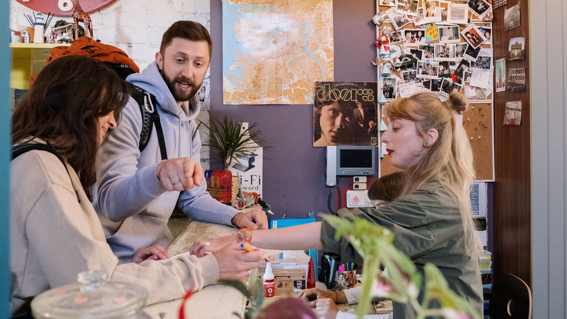 Guests checking in at a hostel reception with a warm interaction between a couple and staff.