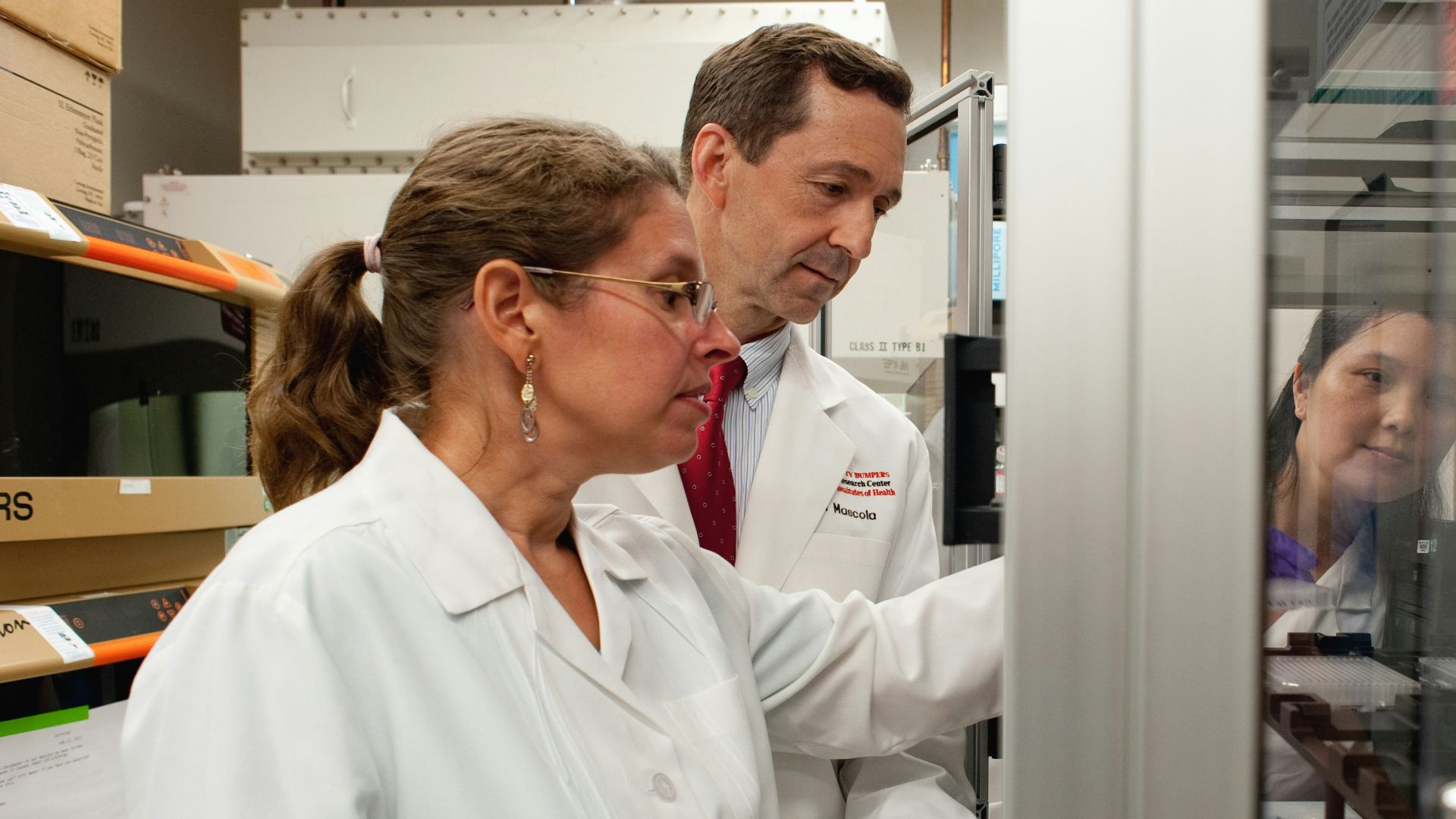 a man and a woman in lab coats looking at something in a cabinet