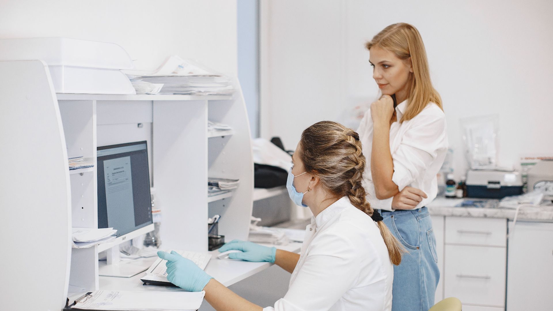 Two female healthcare workers in a clinical office, reviewing diagnostic results on a computer screen.