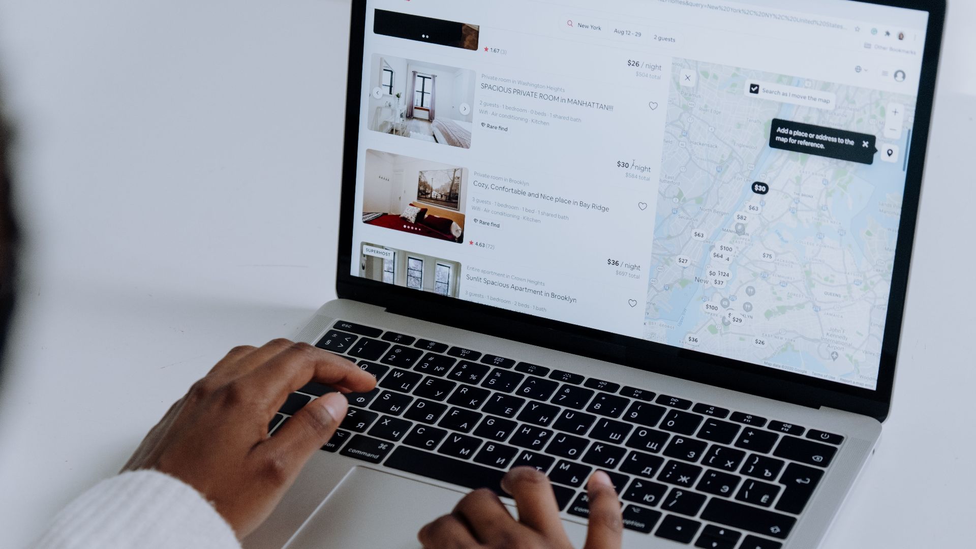 Hands typing on laptop searching Airbnb for accommodation options with map view.