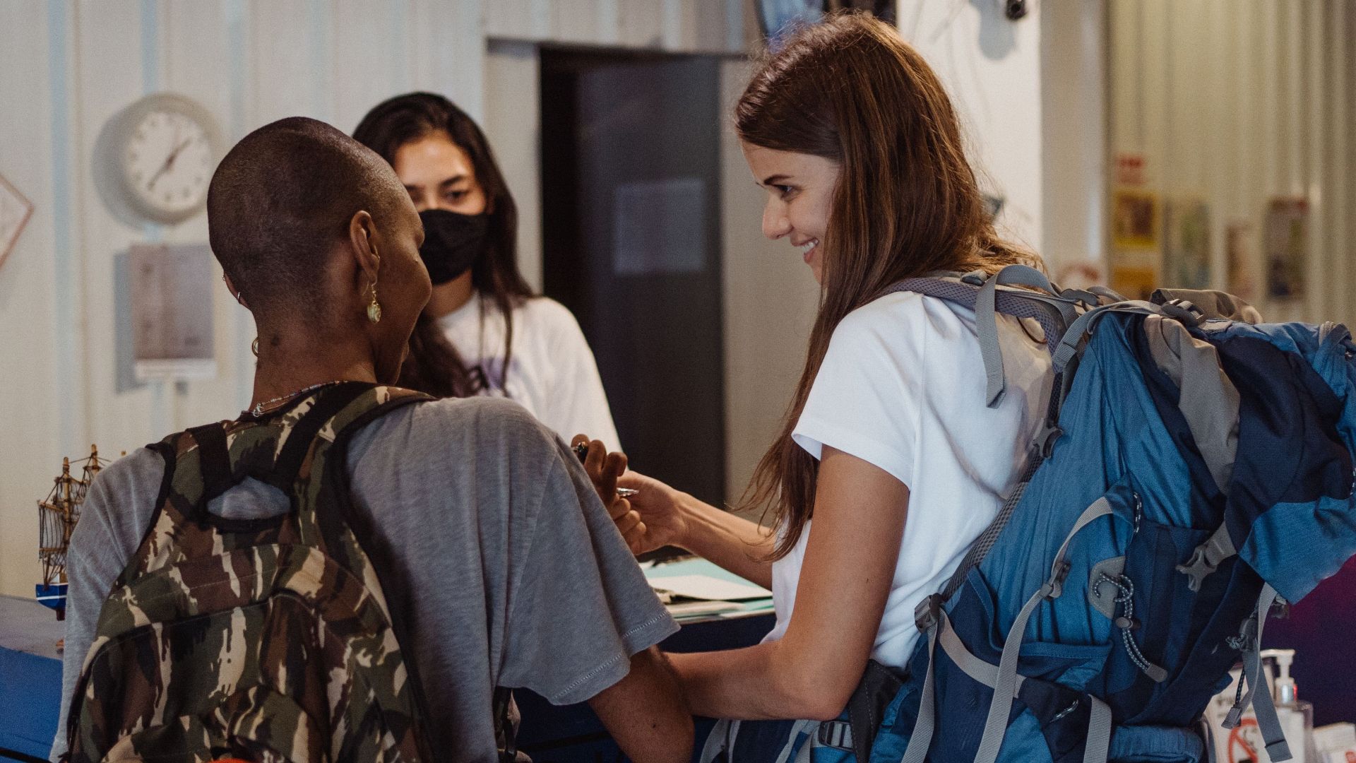 Diverse travelers with backpacks checking in at a lively hostel reception.
