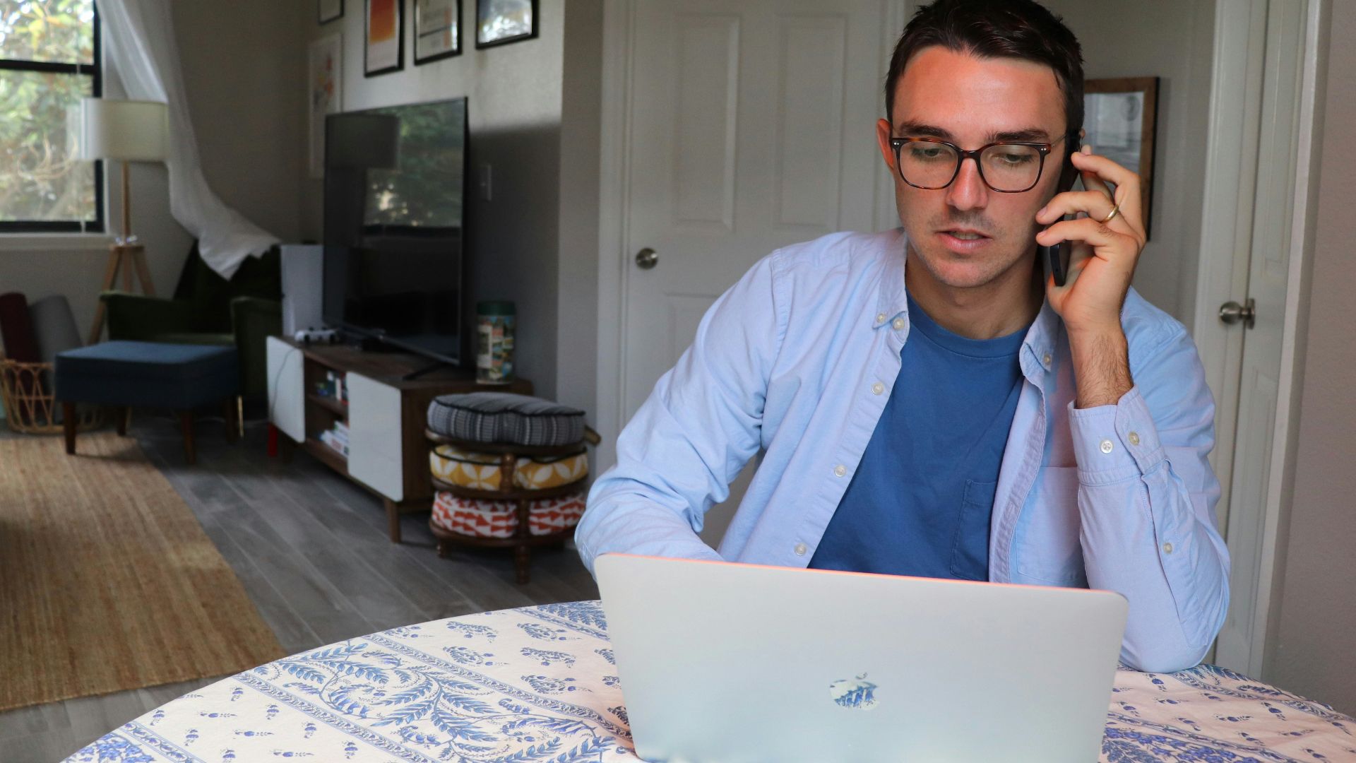 man in white dress shirt wearing eyeglasses sitting by the table using macbook
