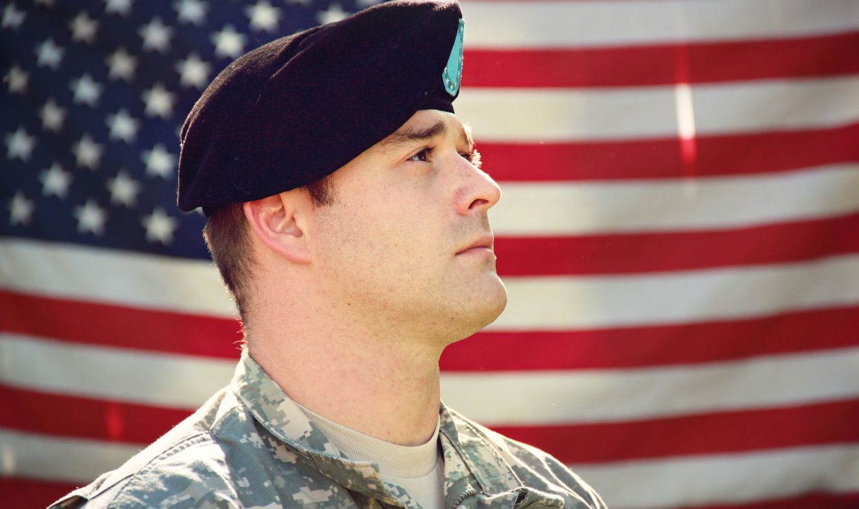 US soldier in uniform stands proudly with the American flag in the background