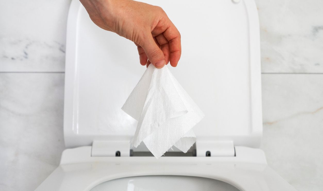 A hand drop wet paper tissue in toilet bowl, flushing water. Delicate cleansing, personal hygiene for people with hemorrhoids. Health care concepts, vertical shot