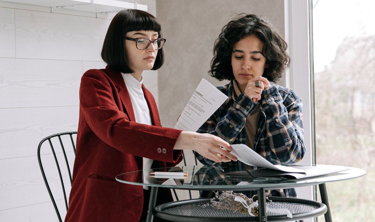 Two women sit at a table reviewing documents in a well-lit modern room