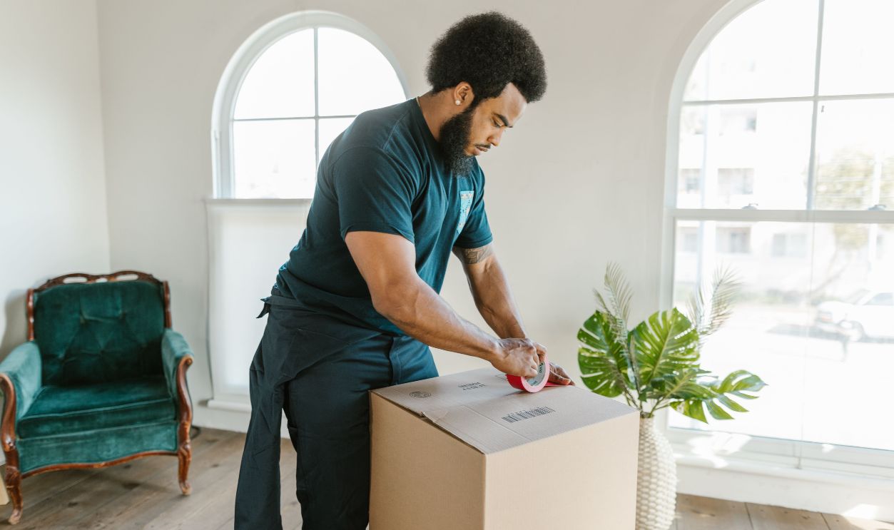A man with afro hair packing a cardboard box in a sunlit room