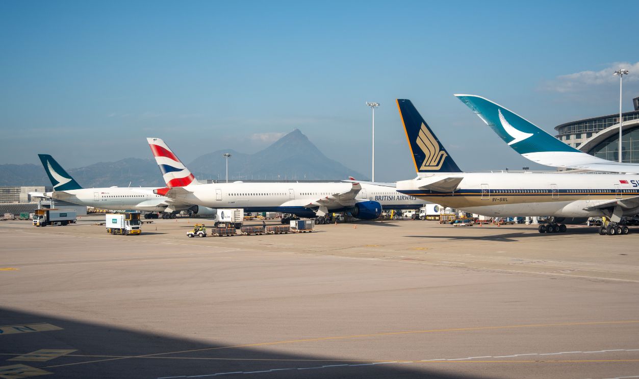 Multiple commercial airplanes parked at an airport terminal with a mountain view in the background