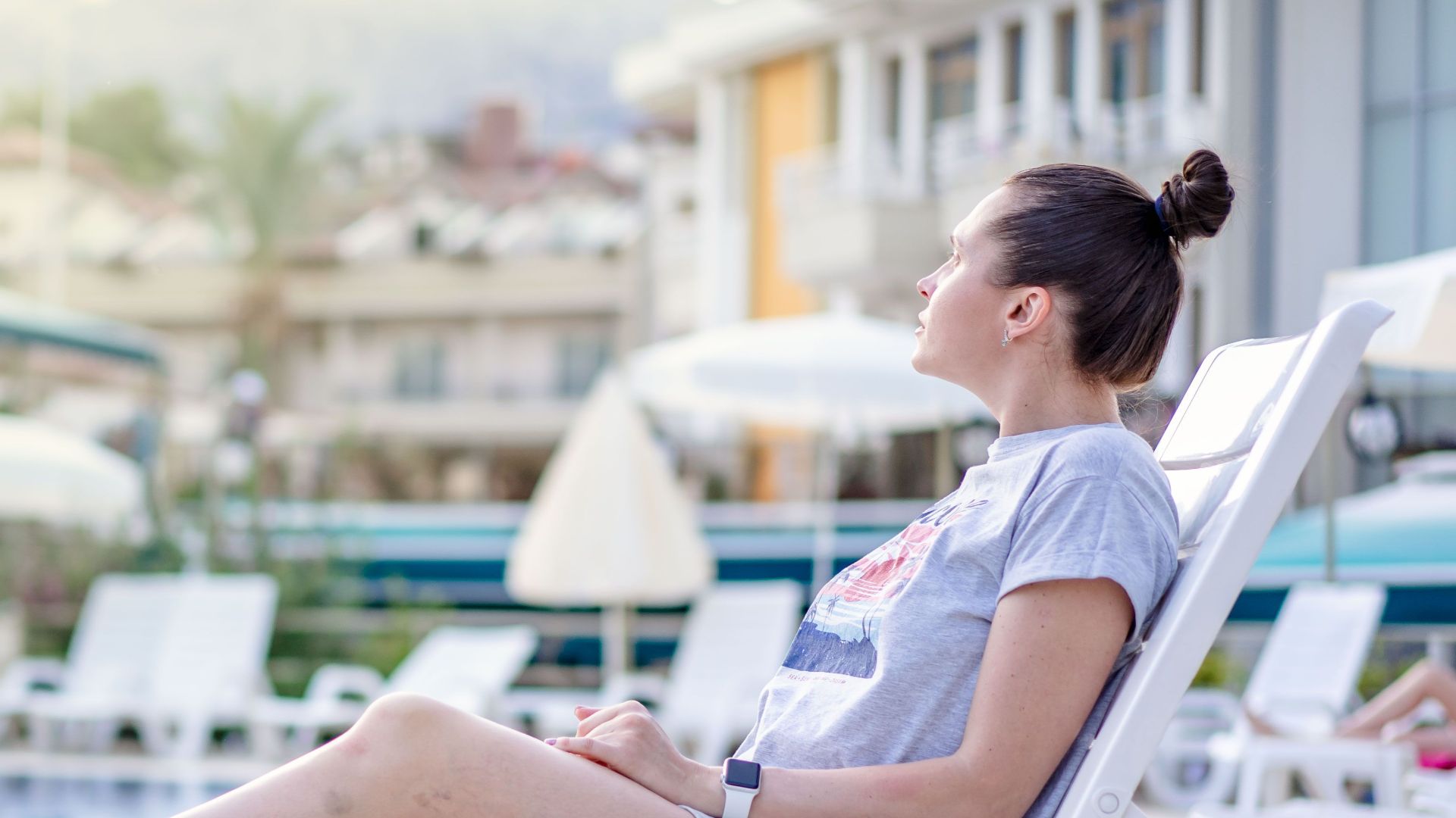 A woman enjoying leisure time on a sun lounger at a poolside resort during summer.
