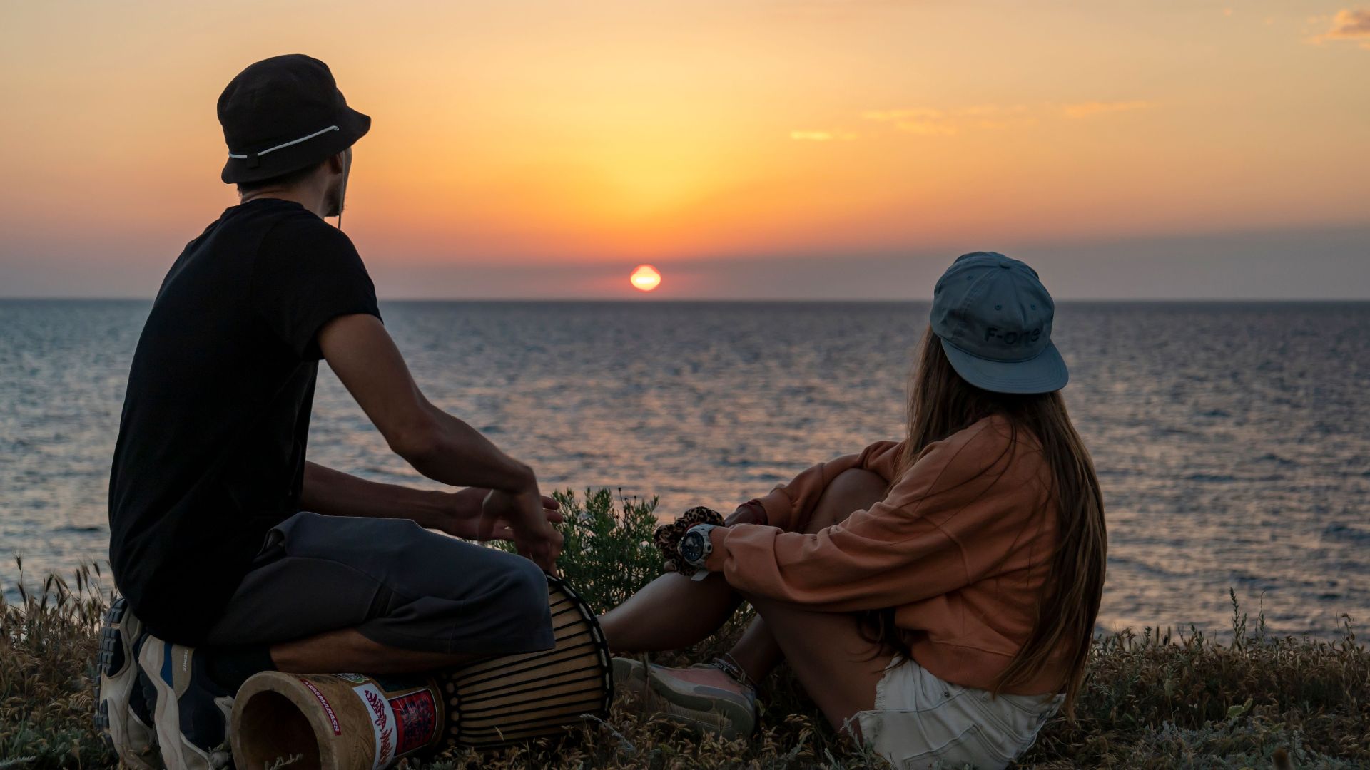 A couple relaxes by the ocean, enjoying a beautiful sunset together, creating a serene and romantic scene.