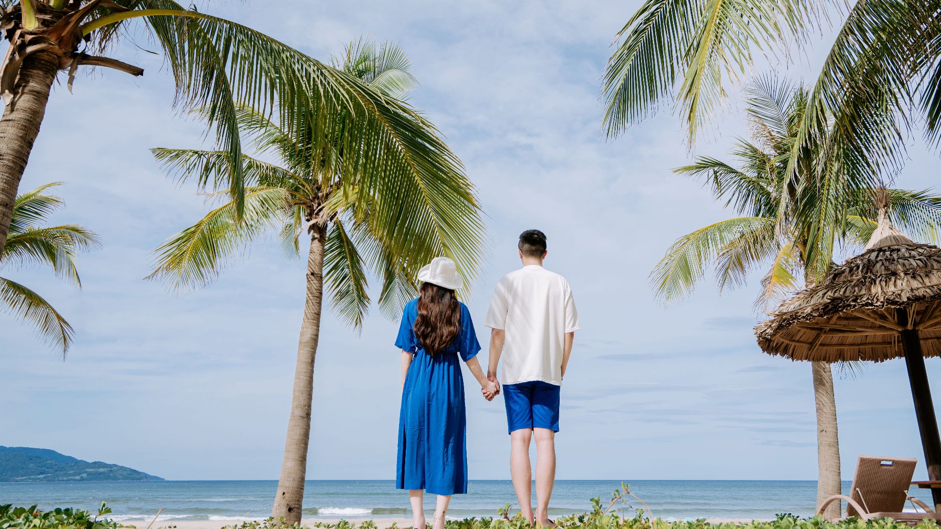 Couple holding hands on a tropical beach surrounded by palm trees, enjoying a serene vacation.