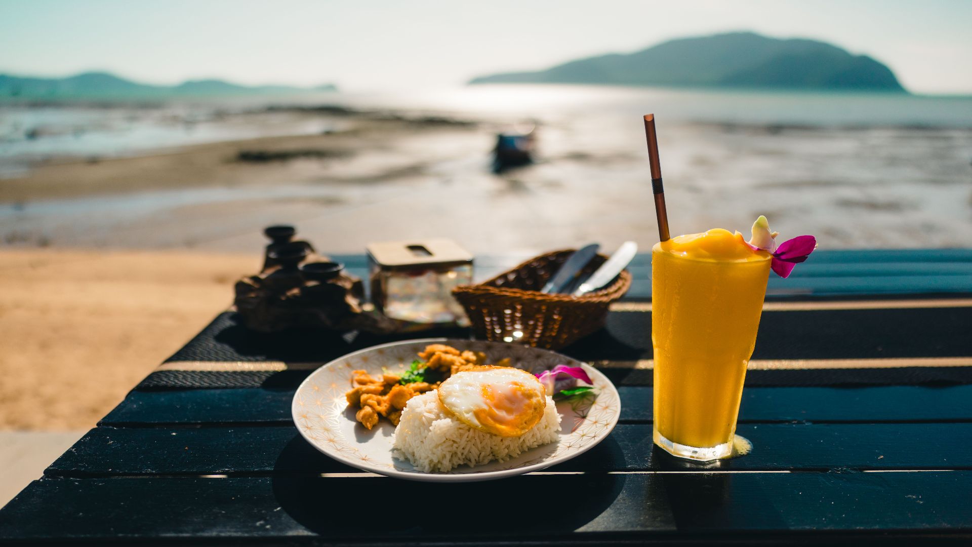 Enjoy a sunny beachside breakfast with rice, eggs, and fresh mango juice in Phuket.