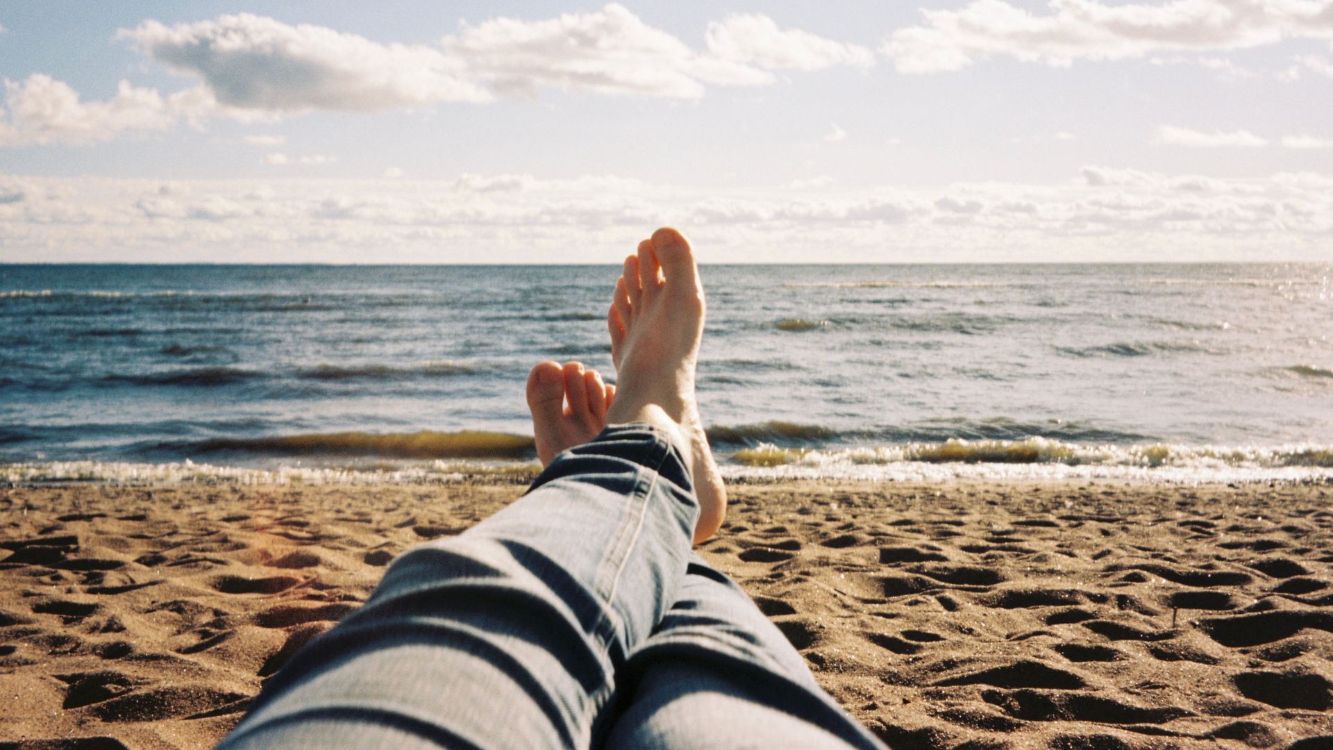 A person relaxing on a sandy beach near the ocean with a clear blue sky.