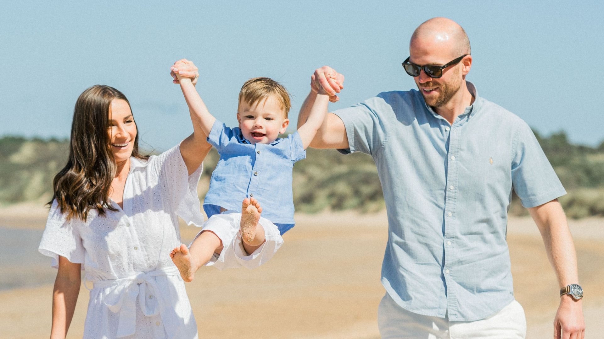 Happy family having fun at the beach, lifting their child in the air.