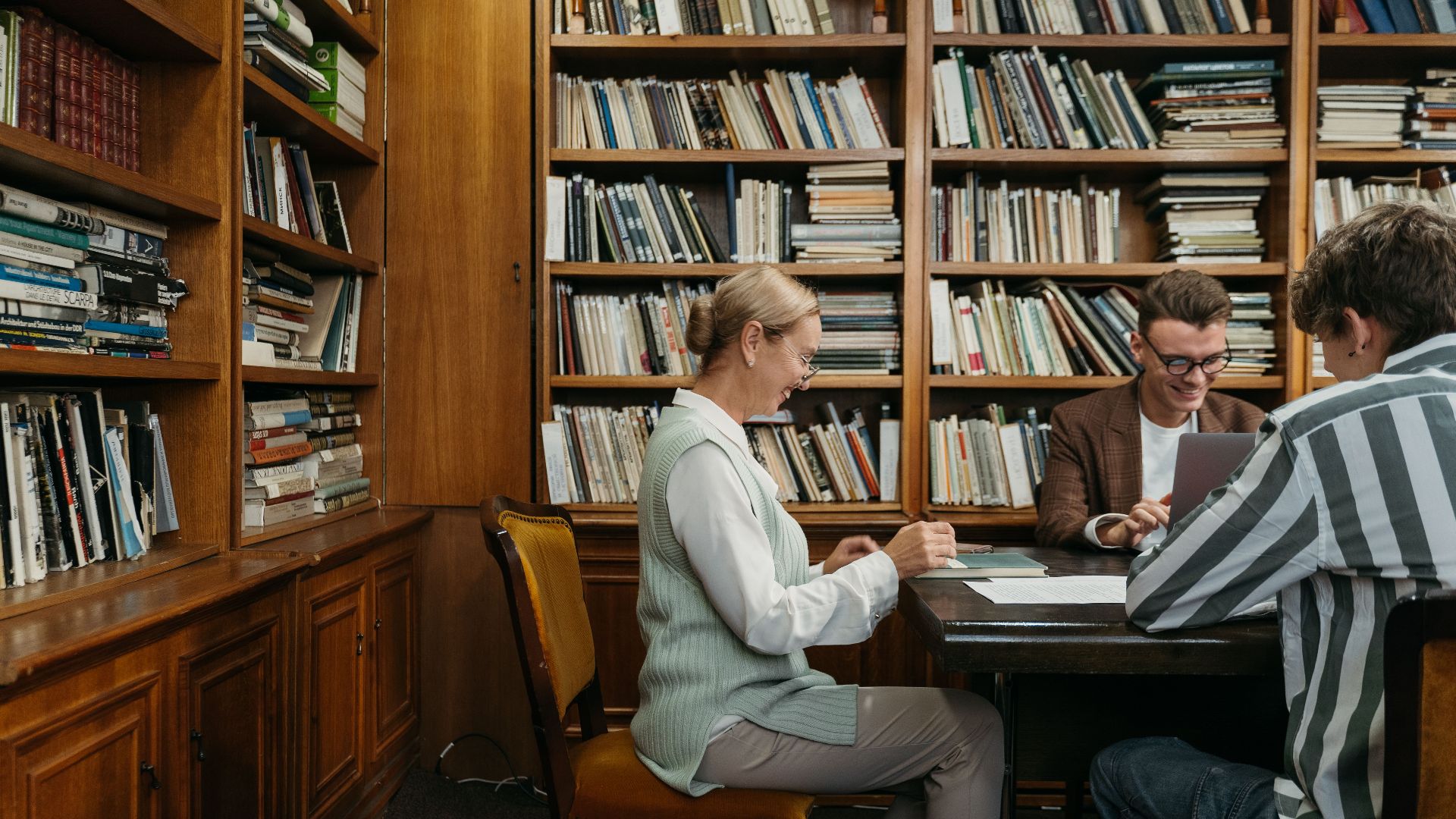 Group of students studying together in a cozy library setting with bookshelves around.