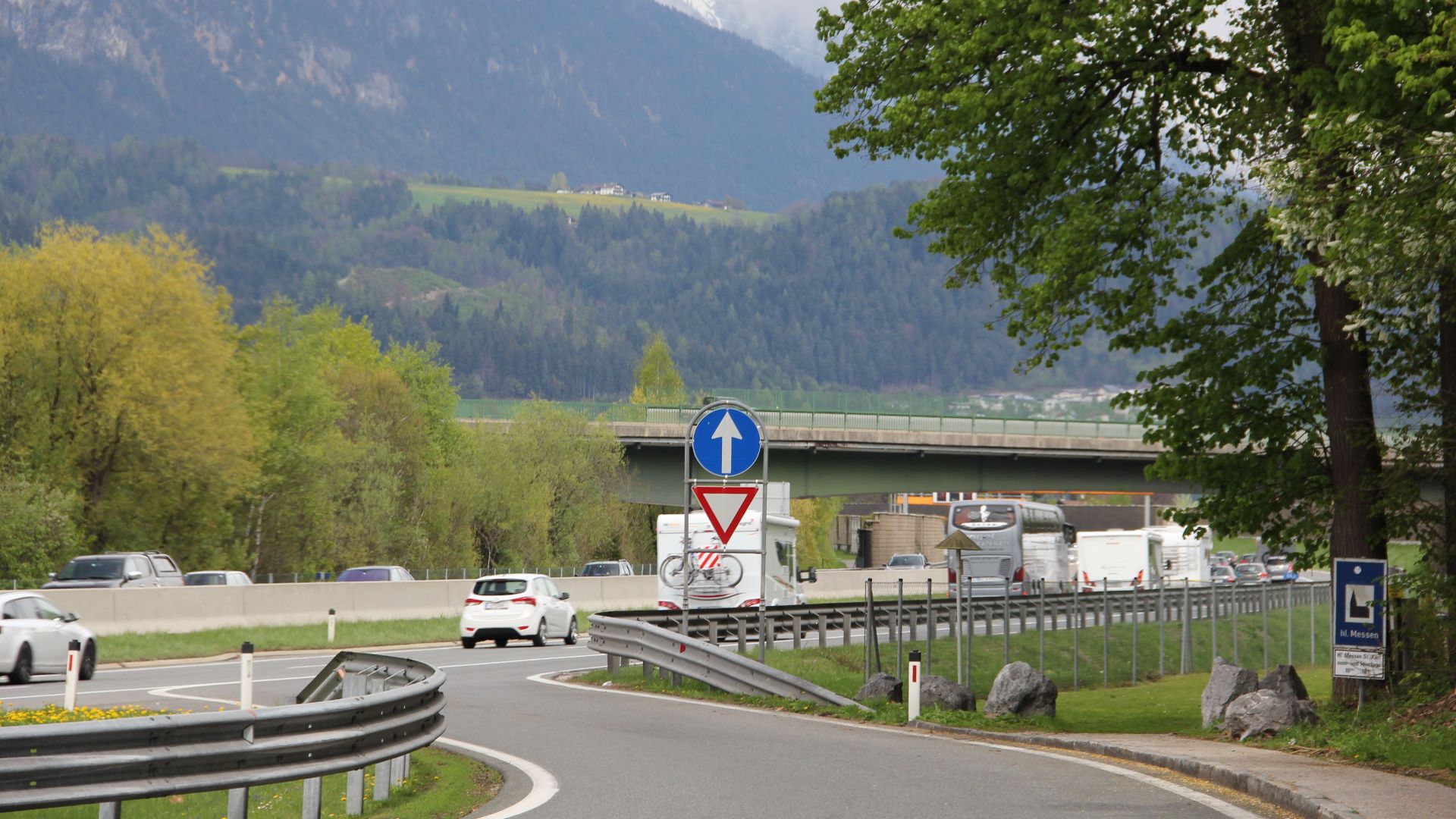 Scenic mountain highway with traffic, lush greenery, and clear sky.