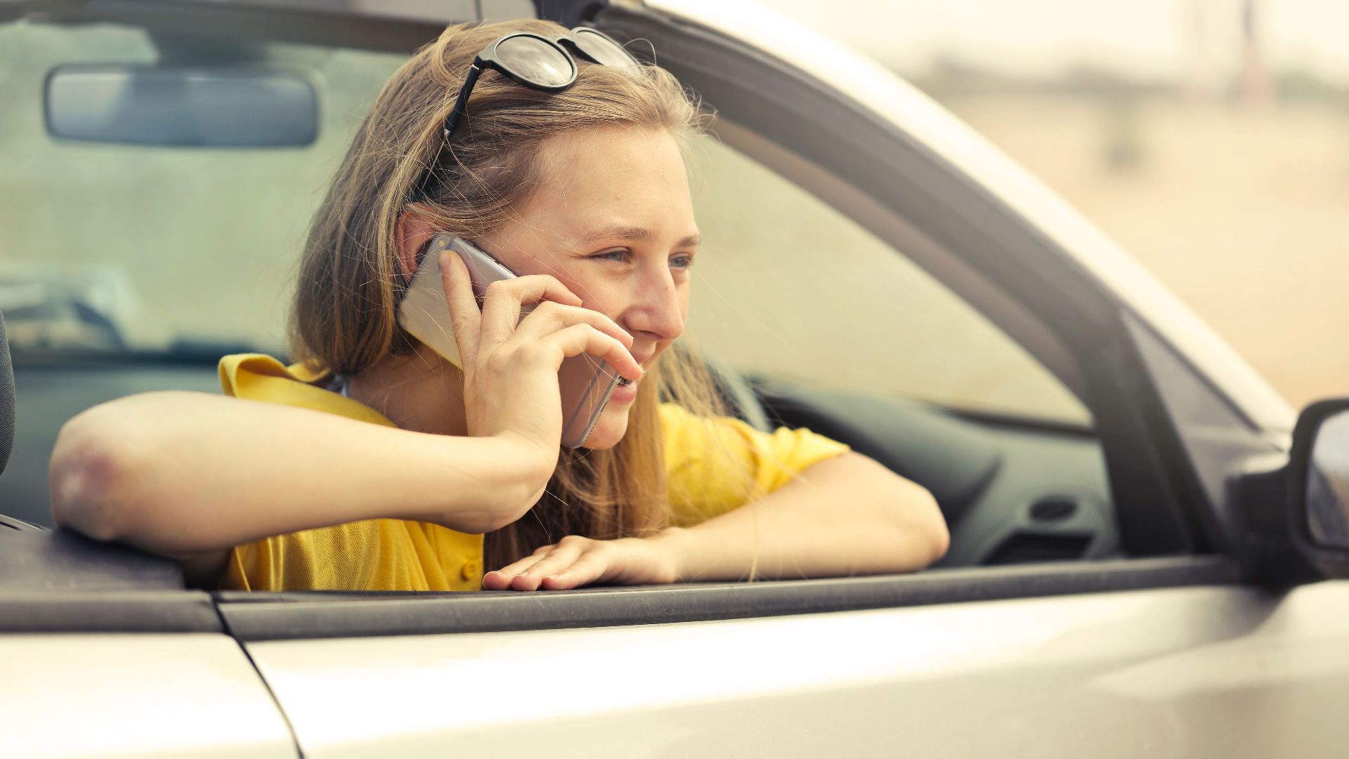 Woman smiling while talking on phone in a convertible car during a sunny day.