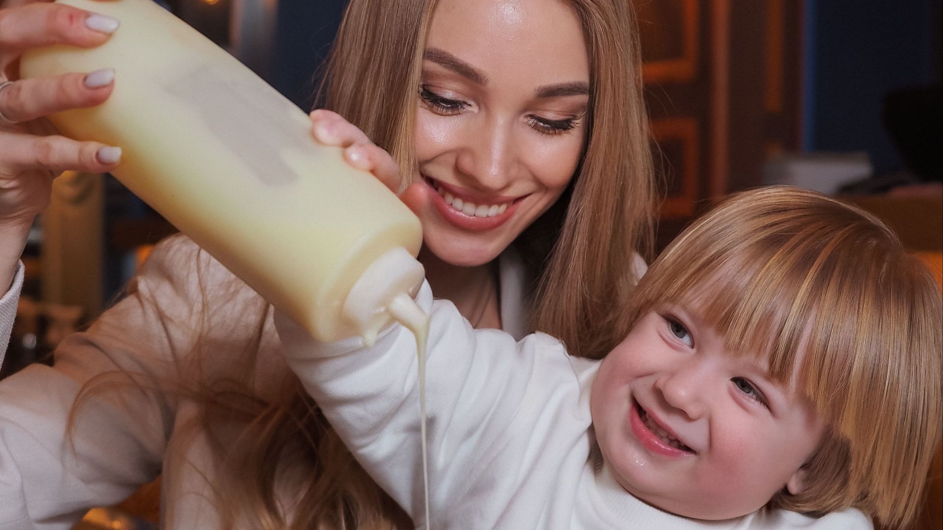A joyful mother and child making breakfast fun by pouring syrup on pancakes.