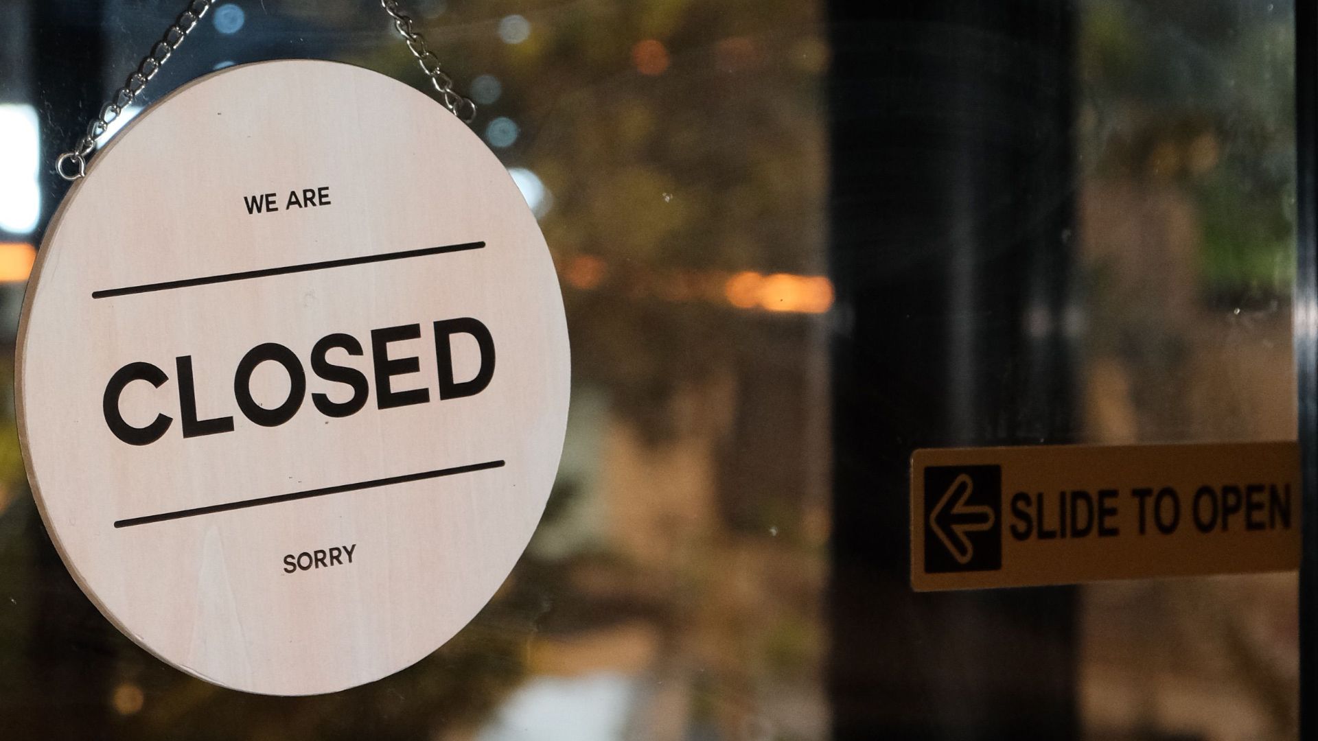 A glass door with a 'Closed' sign in a café at night, signifying closure.