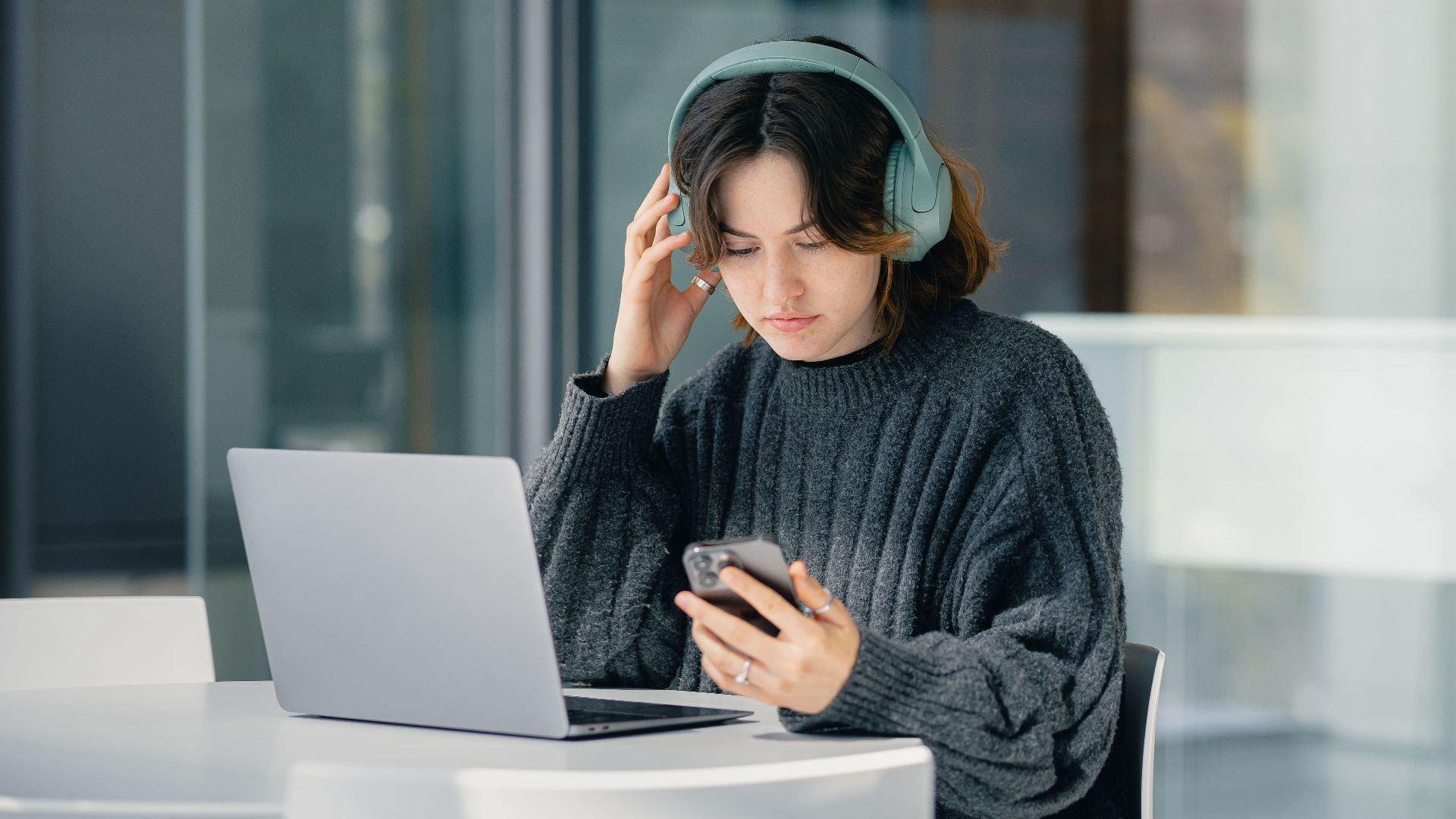 Focused young woman with headphones using laptop and smartphone in a modern cafe.