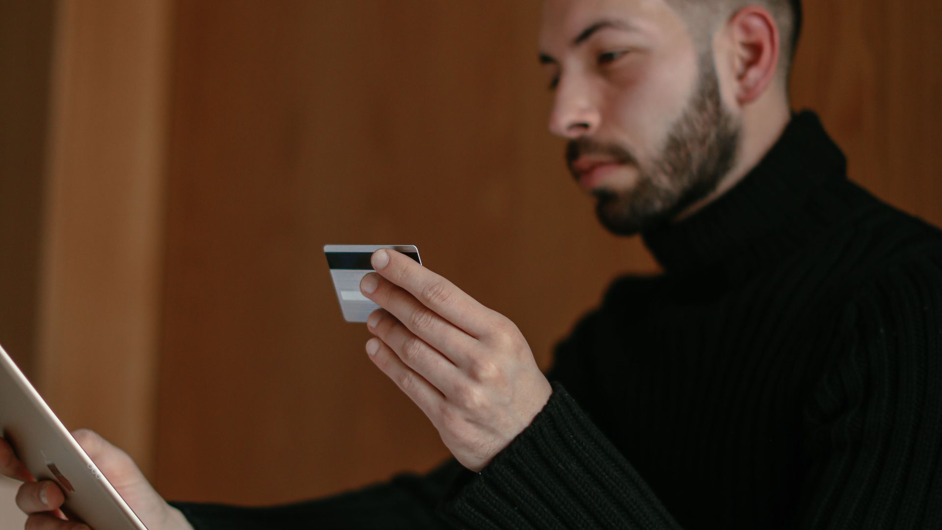 Bearded adult man using a tablet and credit card for online shopping at home.