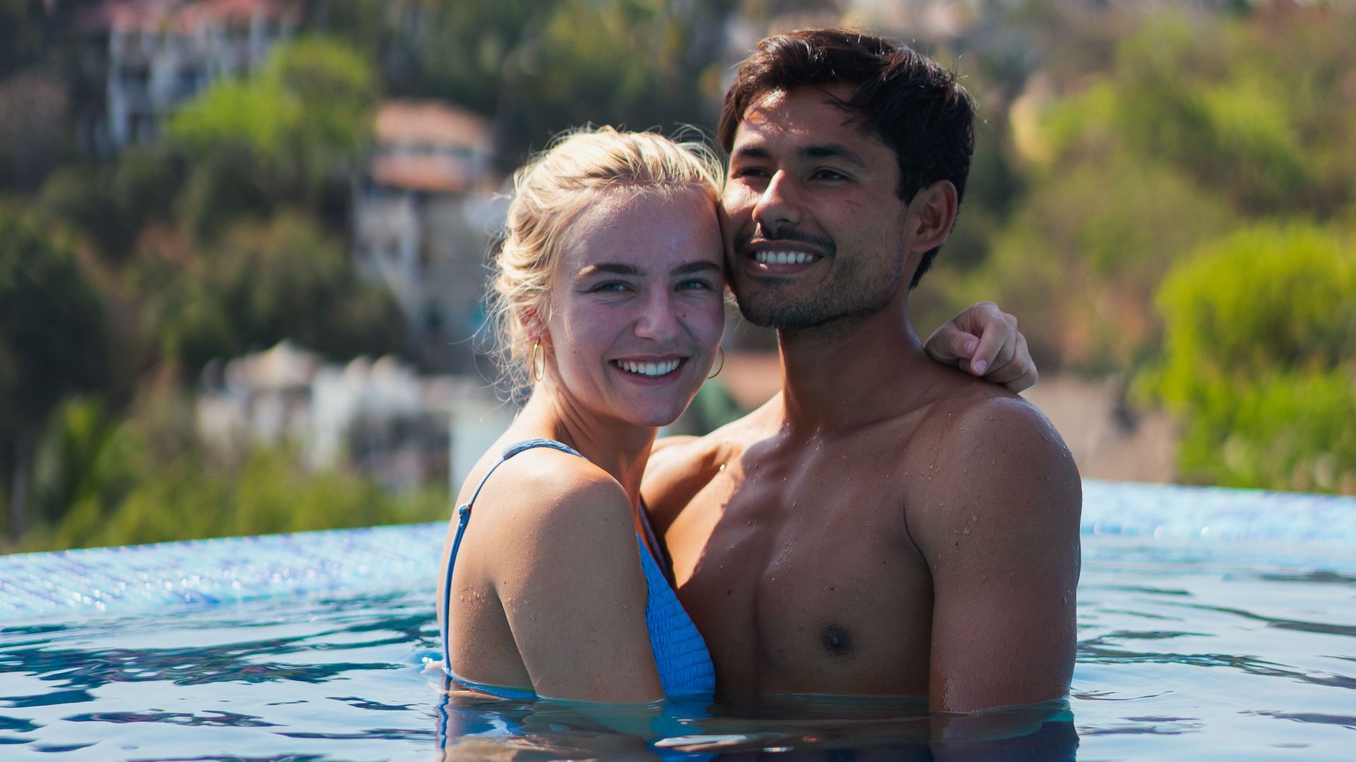 Smiling interracial couple embracing in a serene infinity pool while enjoying a sunny vacation.