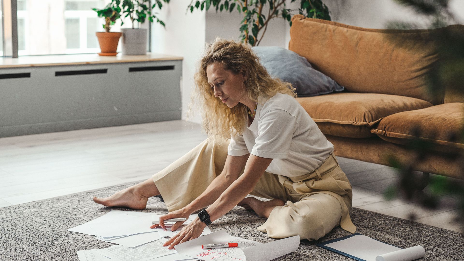A woman sitting on the floor of her living room working on documents and papers, embodying a comfortable work-from-home atmosphere.