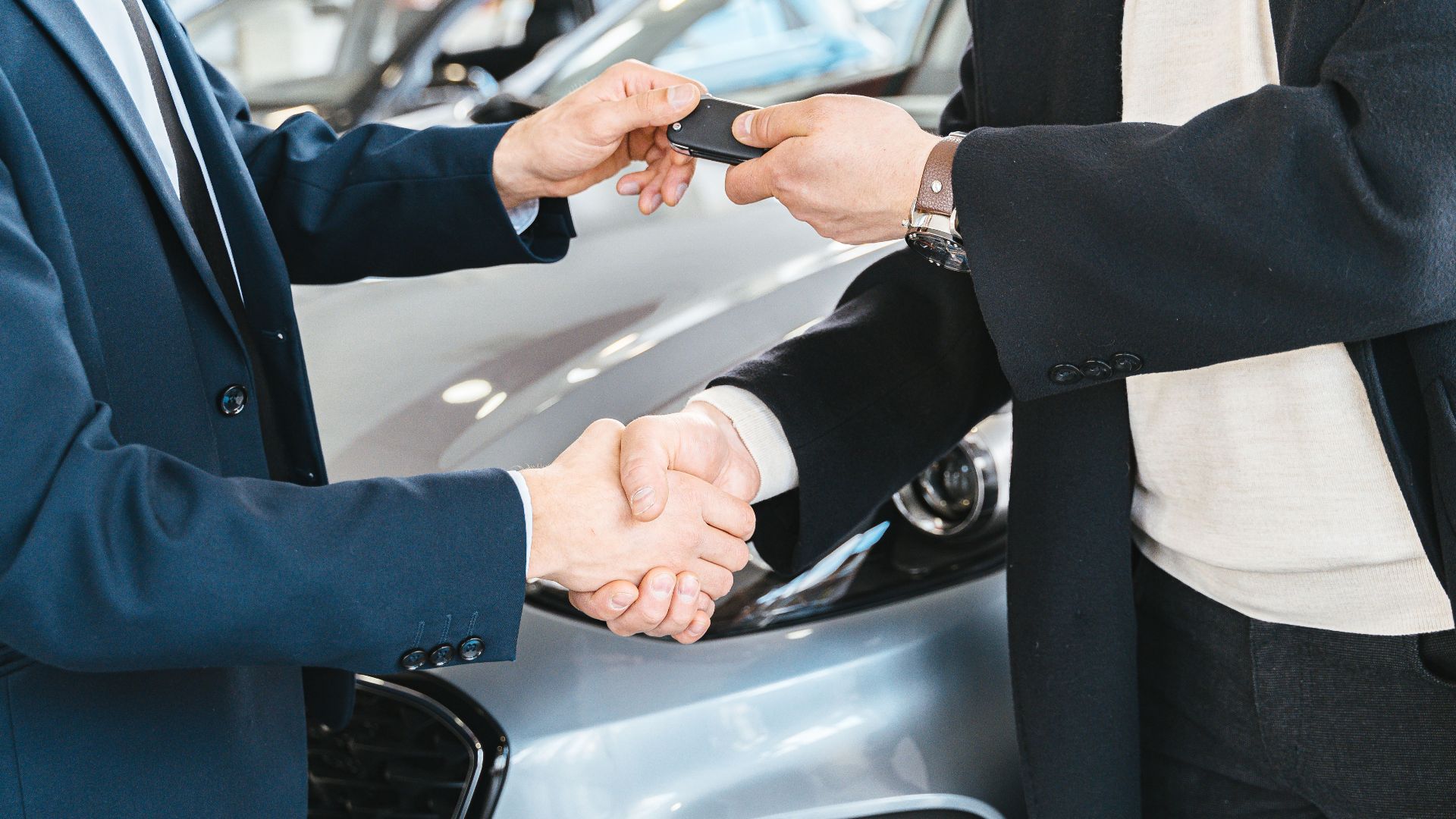 Two businessmen shaking hands and exchanging car keys in a dealership. Symbolizes a successful deal.