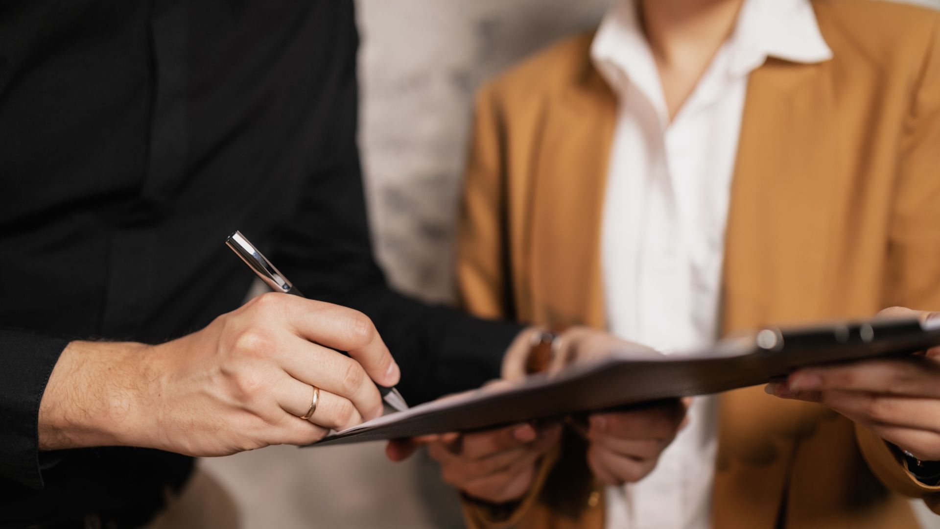 Close-up of two professionals signing a document indoors, focus on hands and pen.