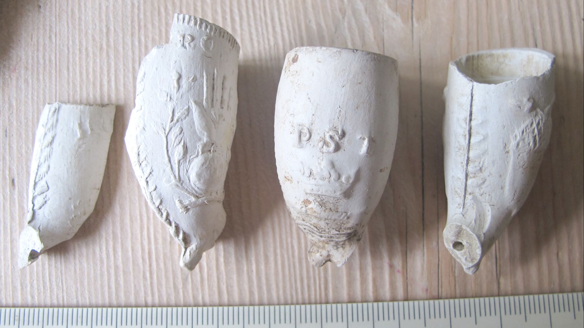 Four modern clay pipe bowls. All are of the decorated English style, circa 1830-60. Far left is of a simple bowl with foliage decoration. Centre-left depicts a bird standing on a globular piece of fruit extending from a branch; the top of the bird extends