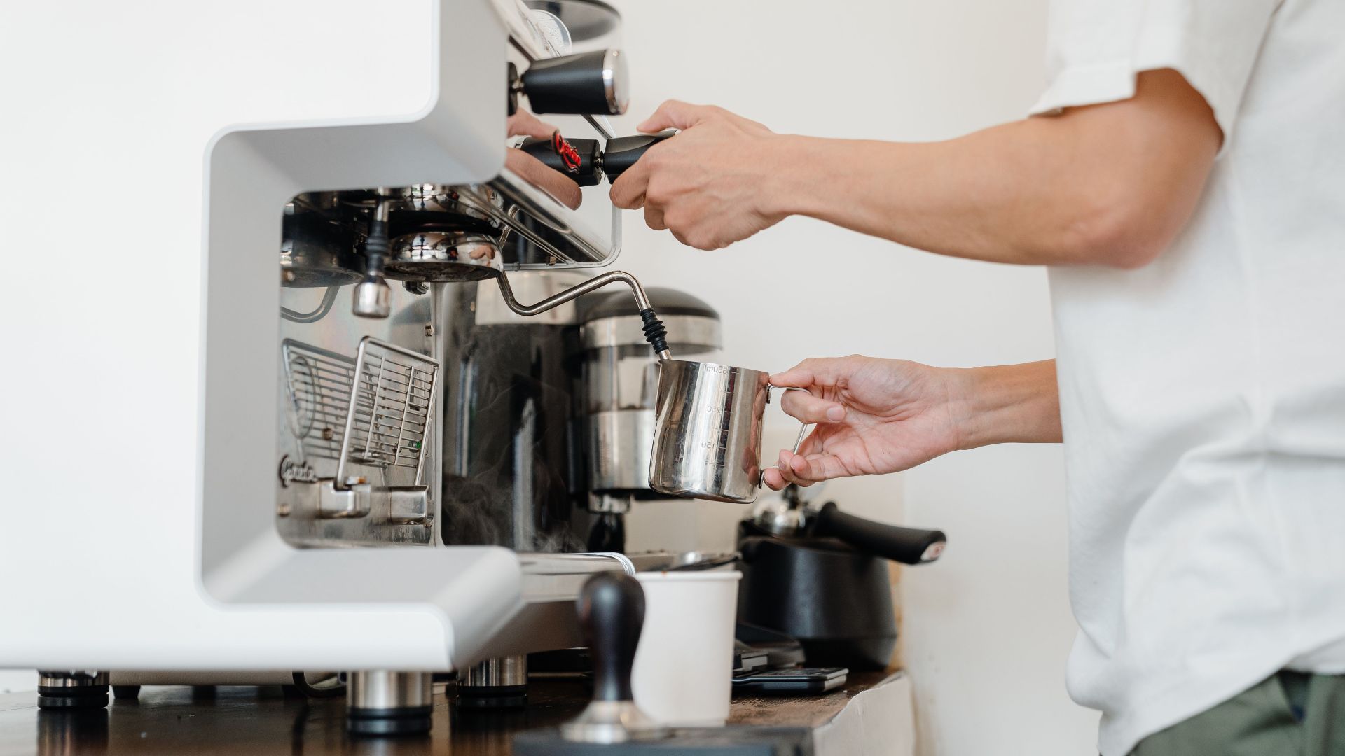 Close-up of a barista steaming milk using an espresso machine in a cafe setting.