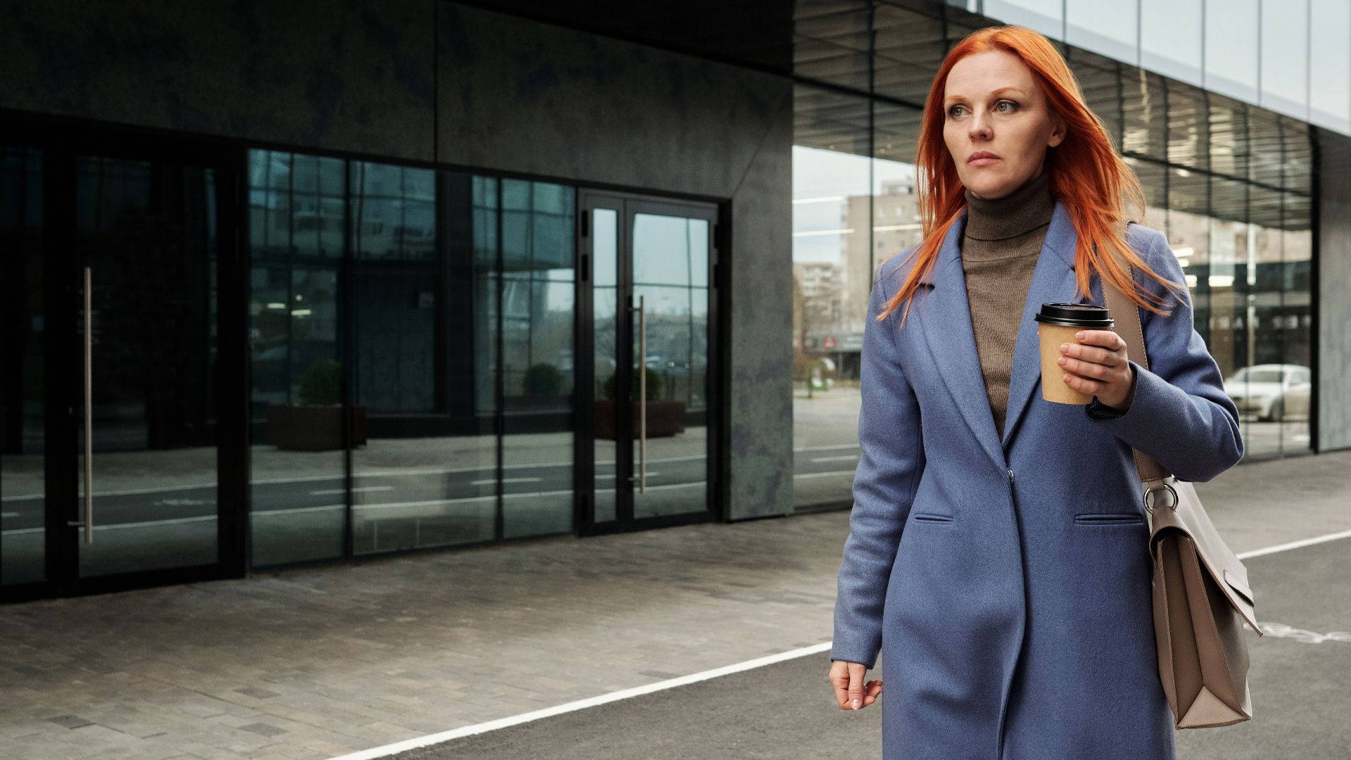 Businesswoman in blue coat walking outside with coffee, exuding confidence.