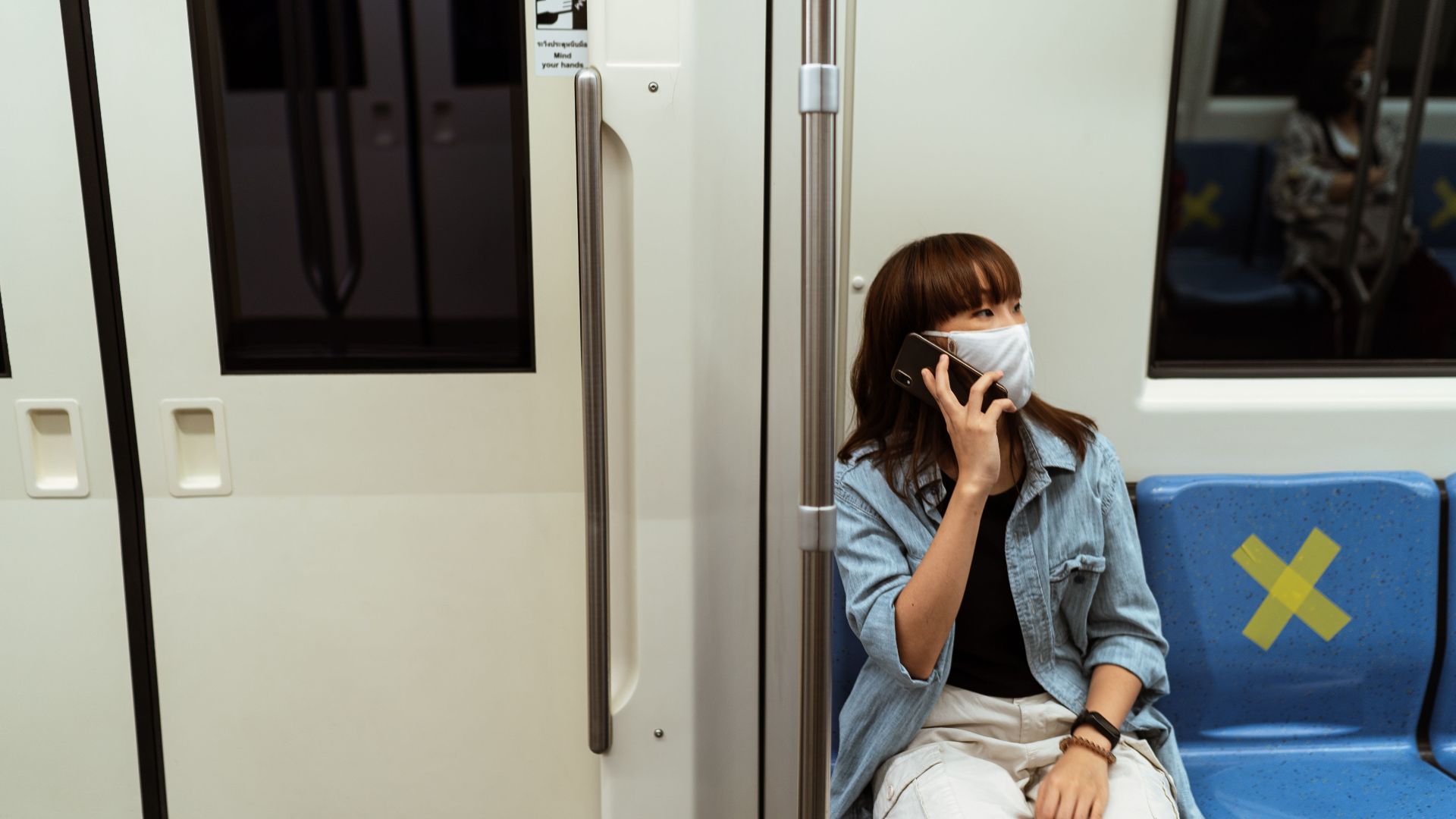 Asian woman wearing a mask talking on phone on an empty subway train.
