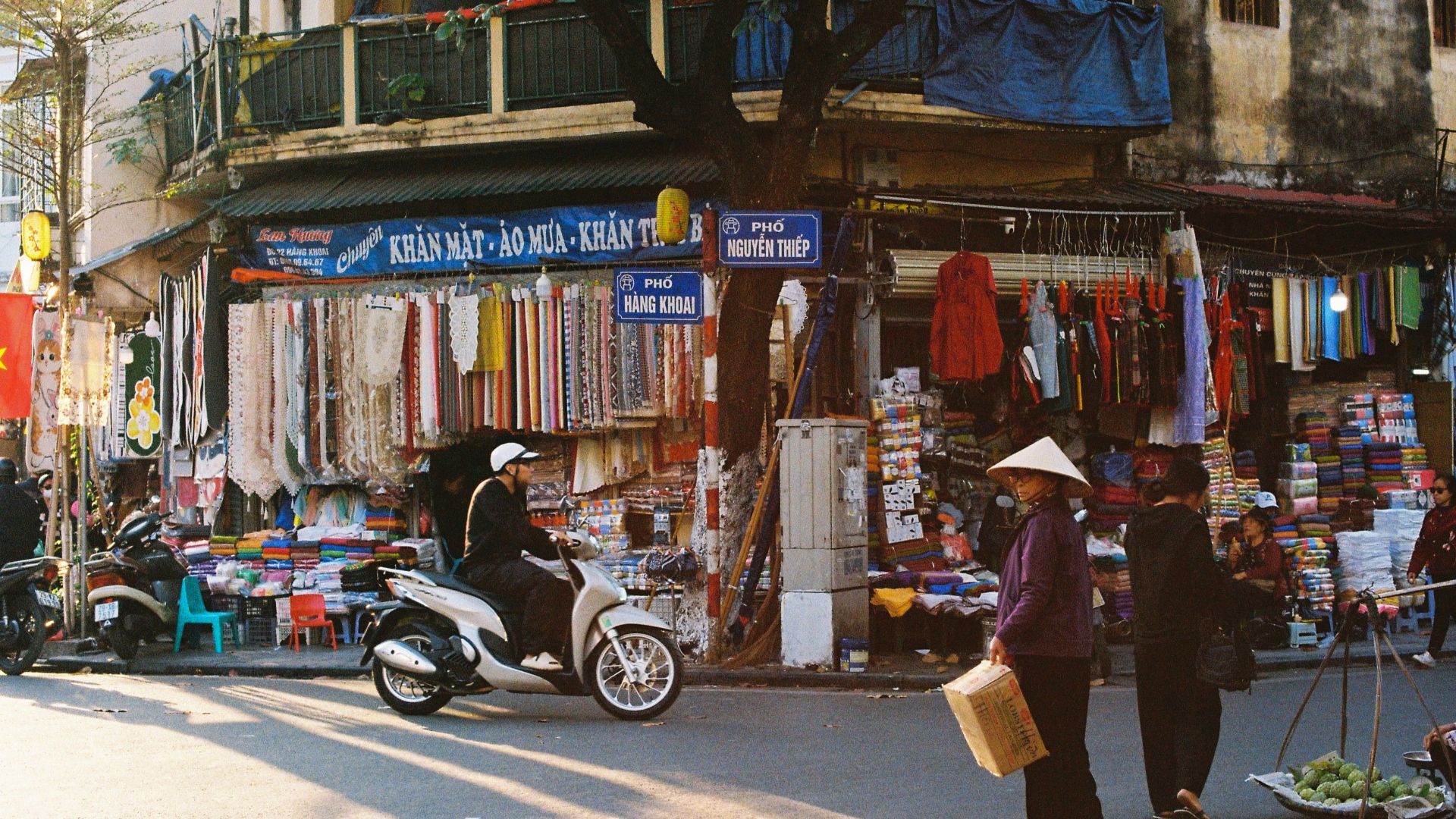 Vibrant street market in Hanoi, Vietnam with people and colorful fabrics.