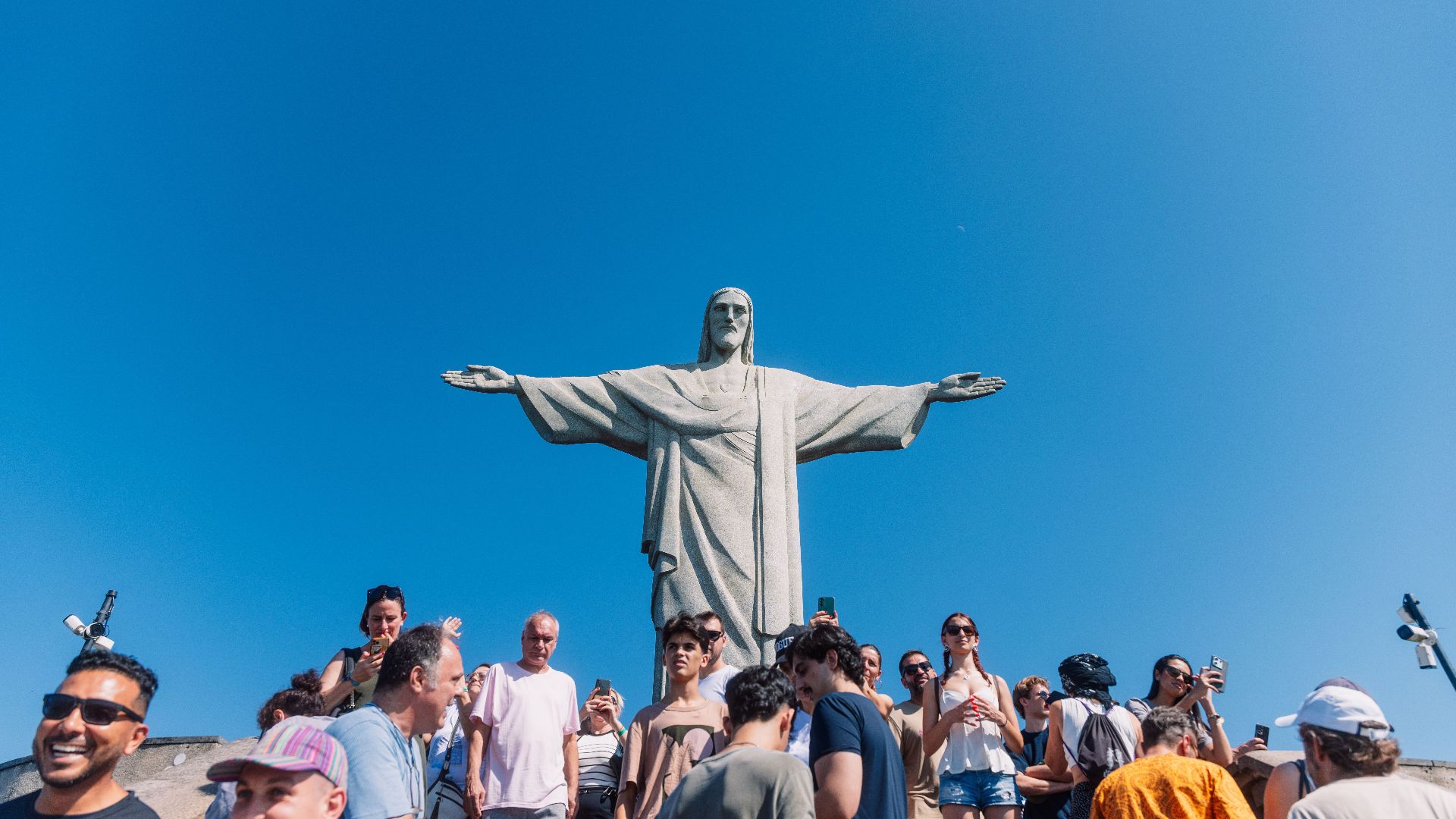 Tourists gather at the iconic Christ the Redeemer statue under clear blue skies in Rio de Janeiro, Brazil.