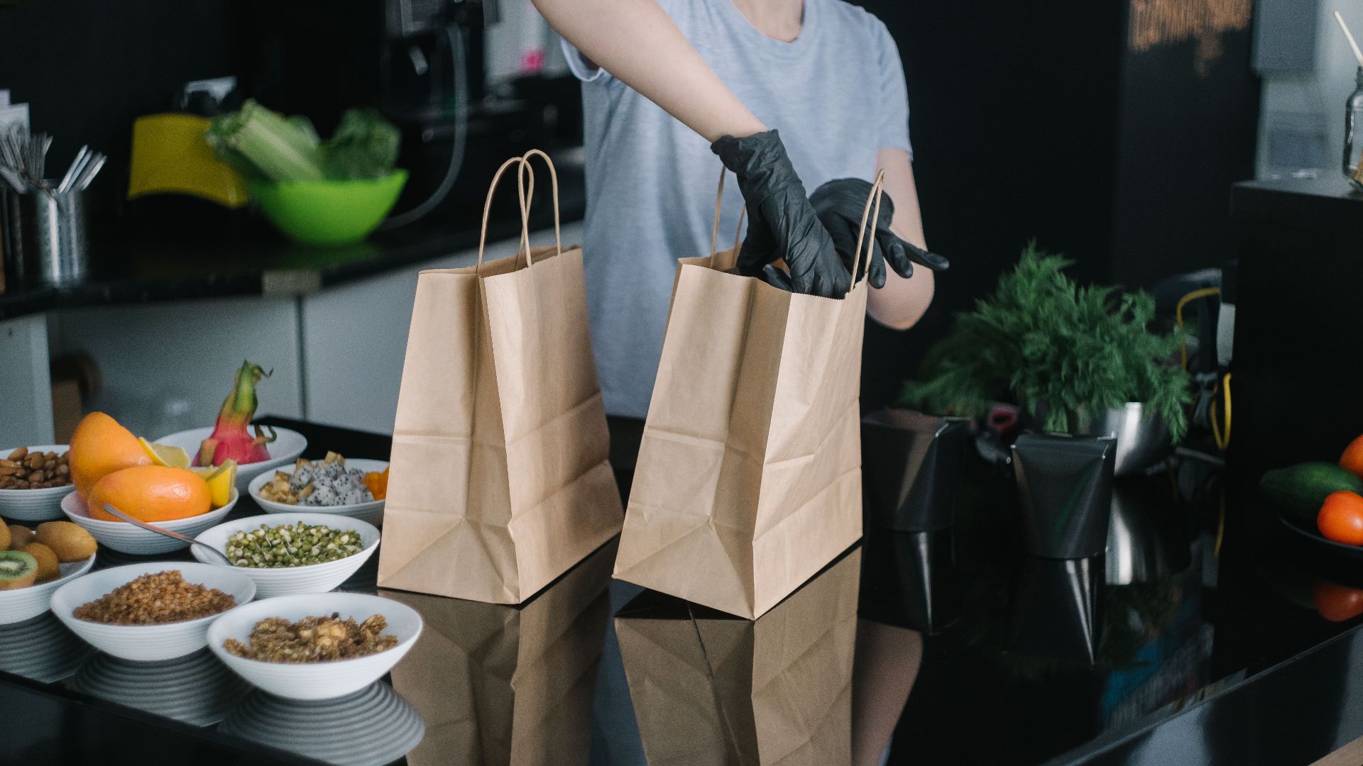 A person in a kitchen packing food ingredients into paper bags for takeout orders.