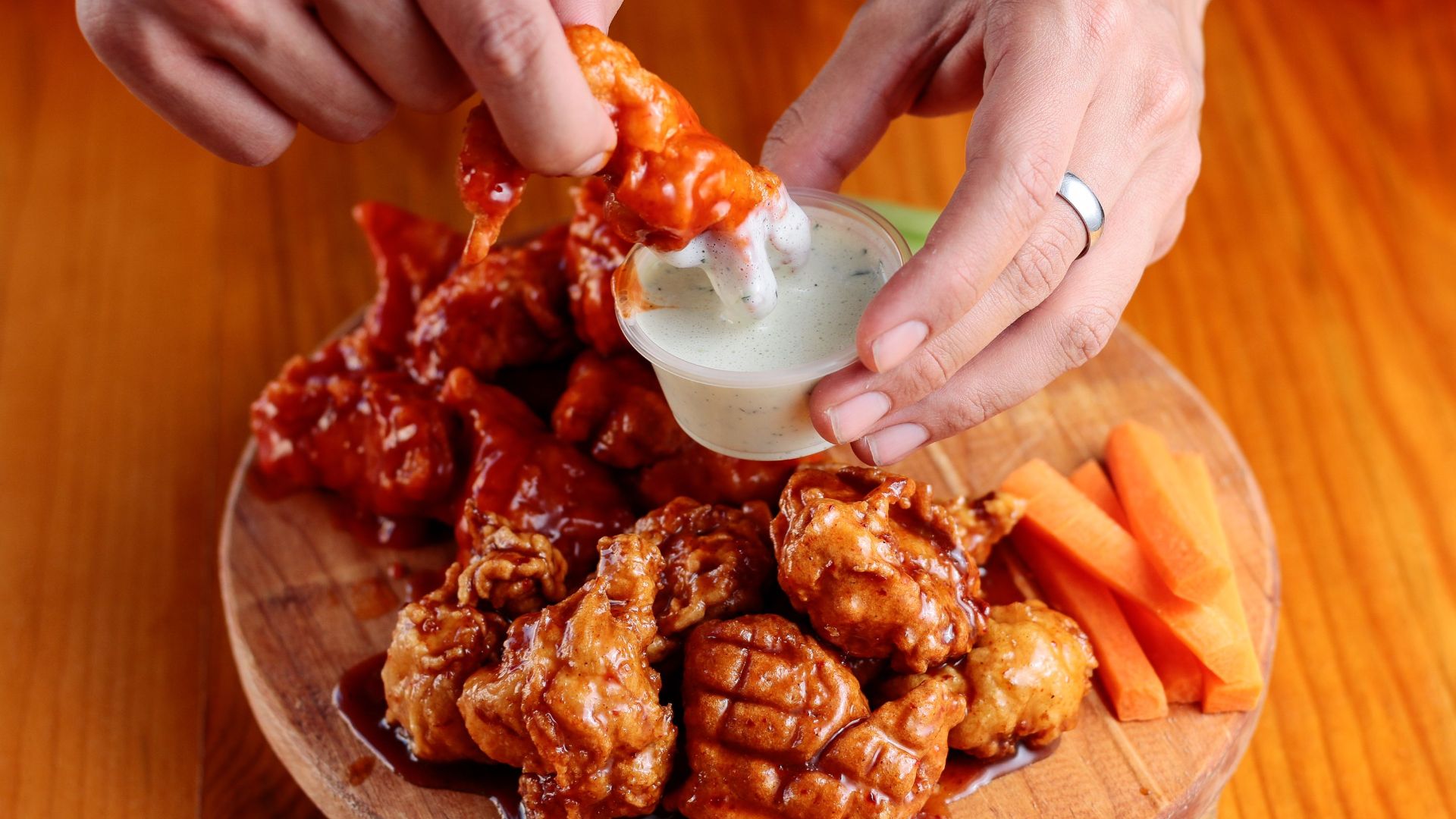 Delicious chicken wings on a wooden platter with dipping sauce and carrot sticks.