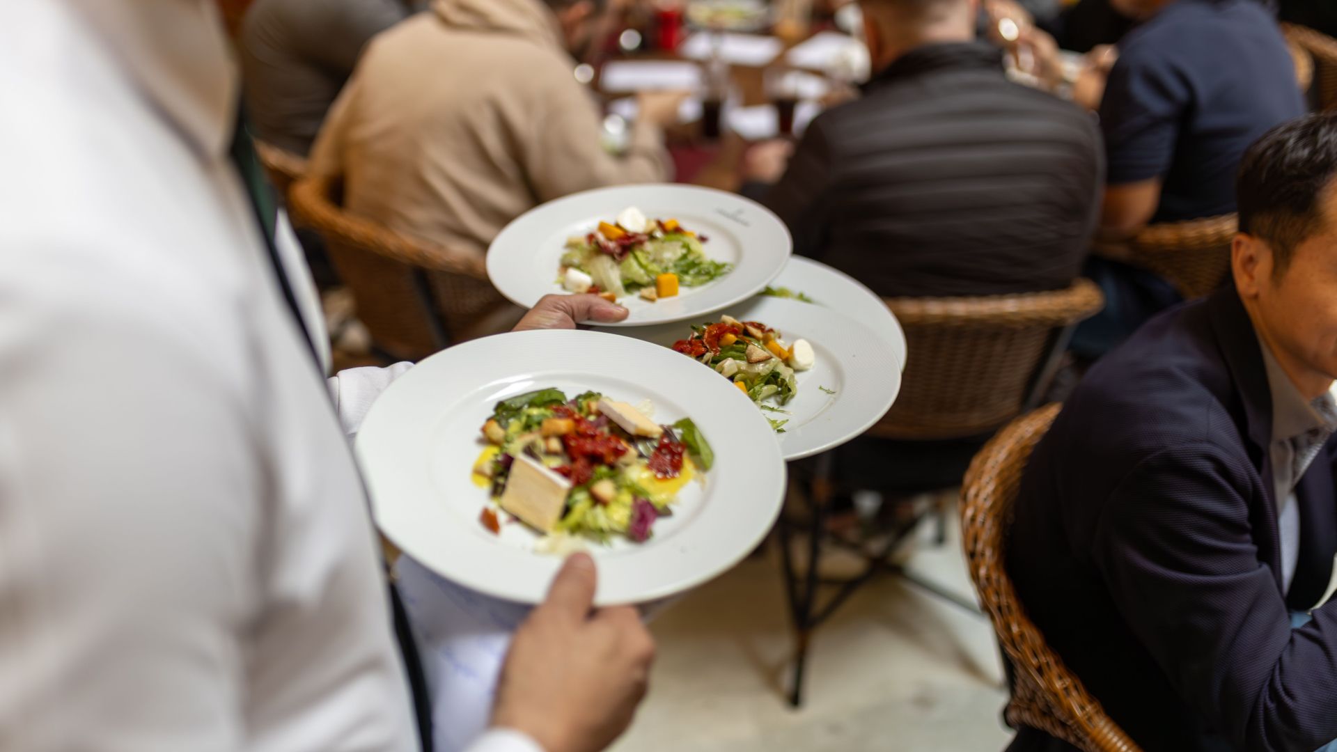 A waiter serves gourmet salads to a group of diners in a lively restaurant setting.