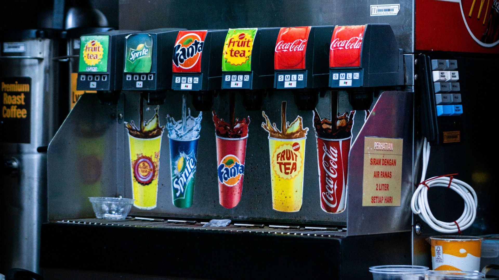 Soft drink dispenser with various soda options in fast food restaurant.
