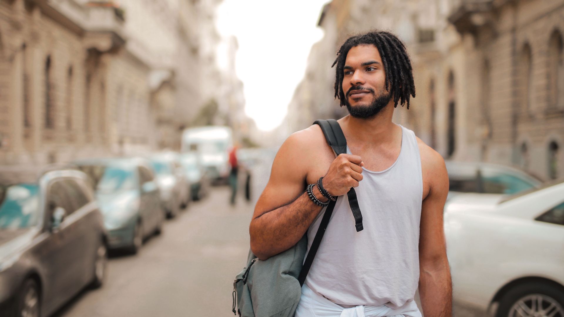 Stylish young man walking through an urban street, enjoying a sunny day outdoors.