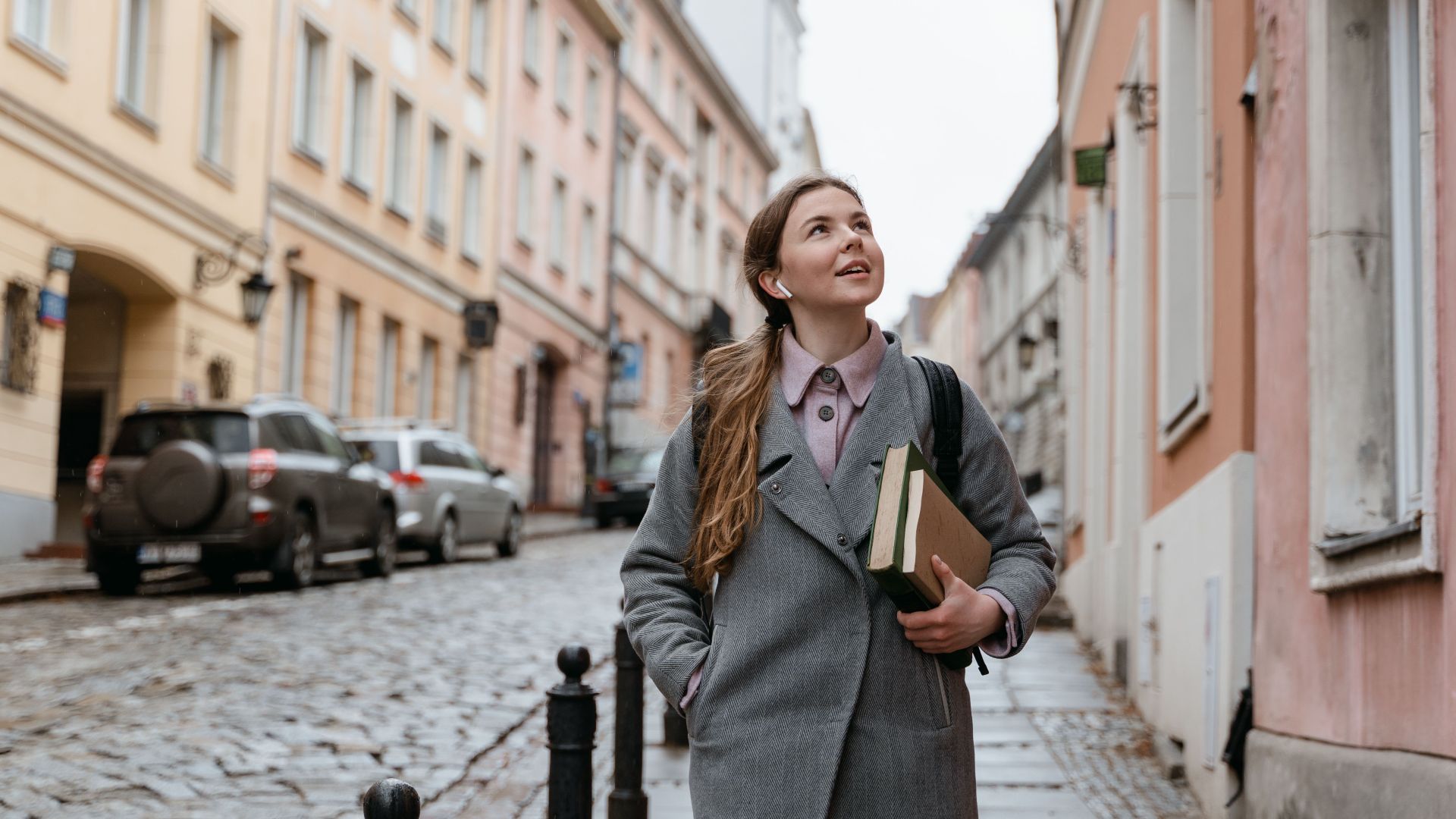 A young woman enjoys walking in a charming cobblestone city street lined with historic buildings.