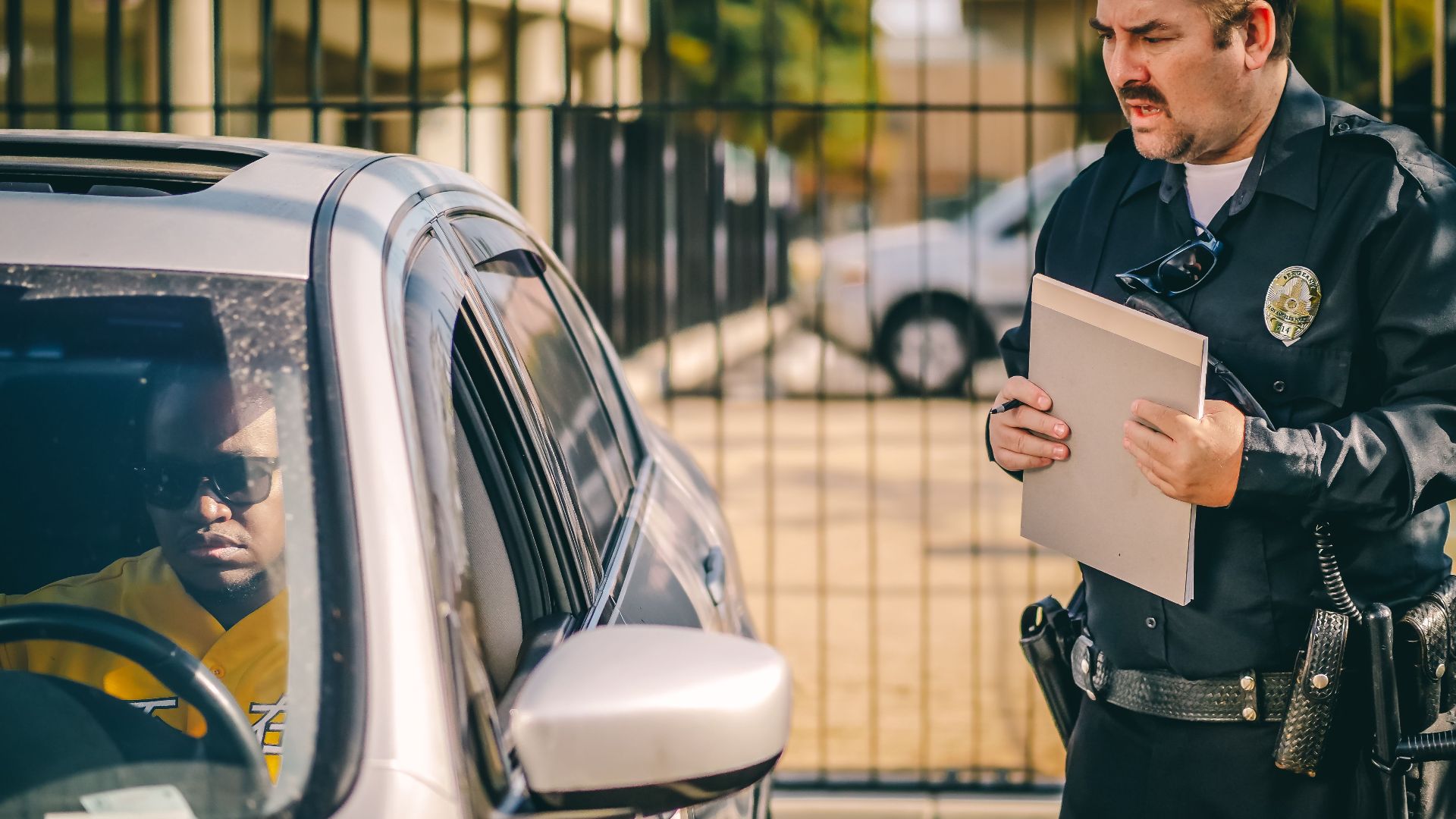 Police officer at car window issuing a ticket to a driver in a sunny outdoor setting.