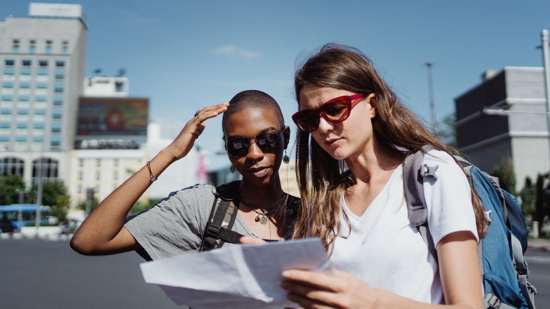 Two women tourists checking a map while exploring a city on a sunny day.