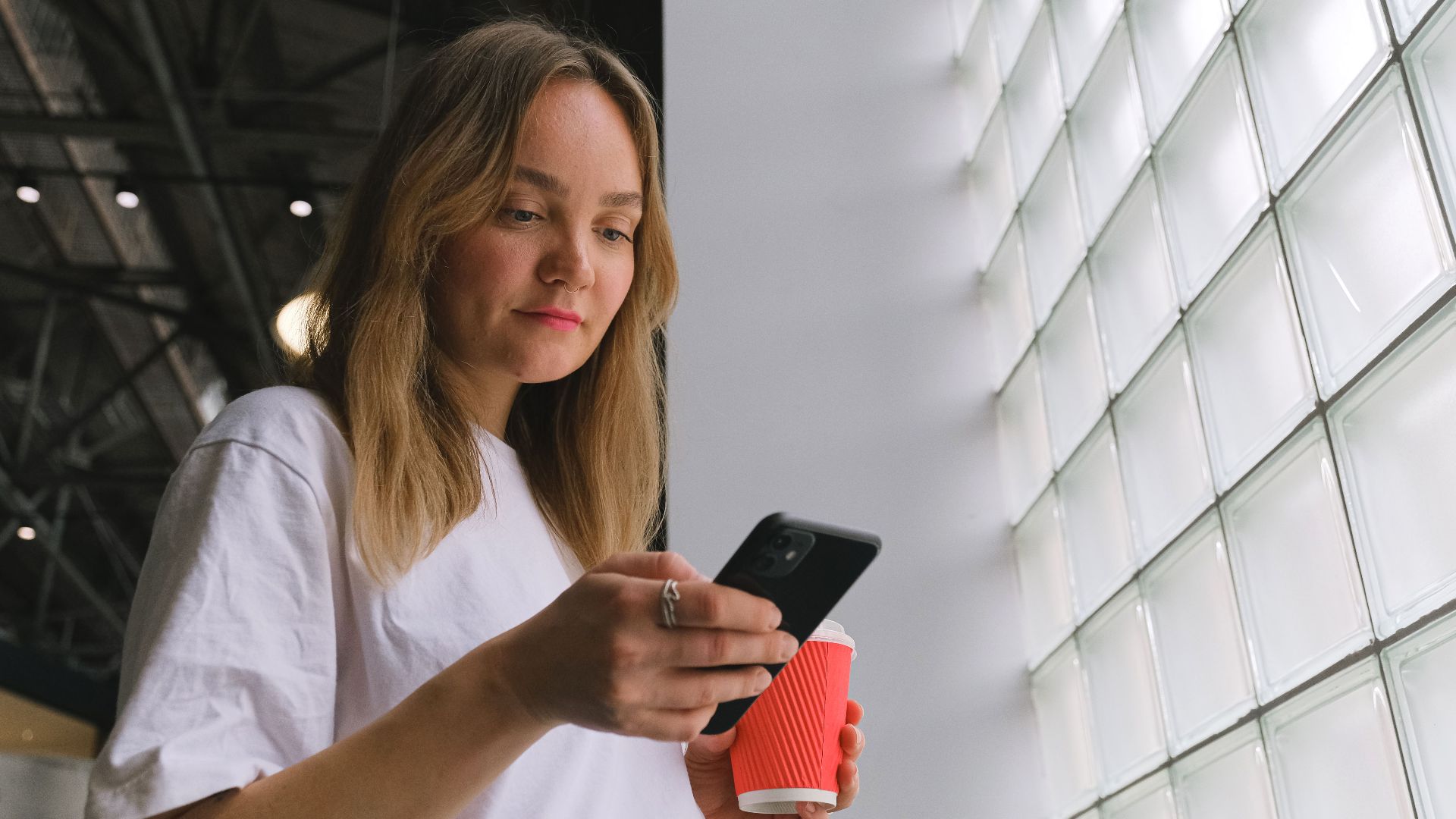 Blonde woman holding a coffee cup and phone indoors with stylish design.