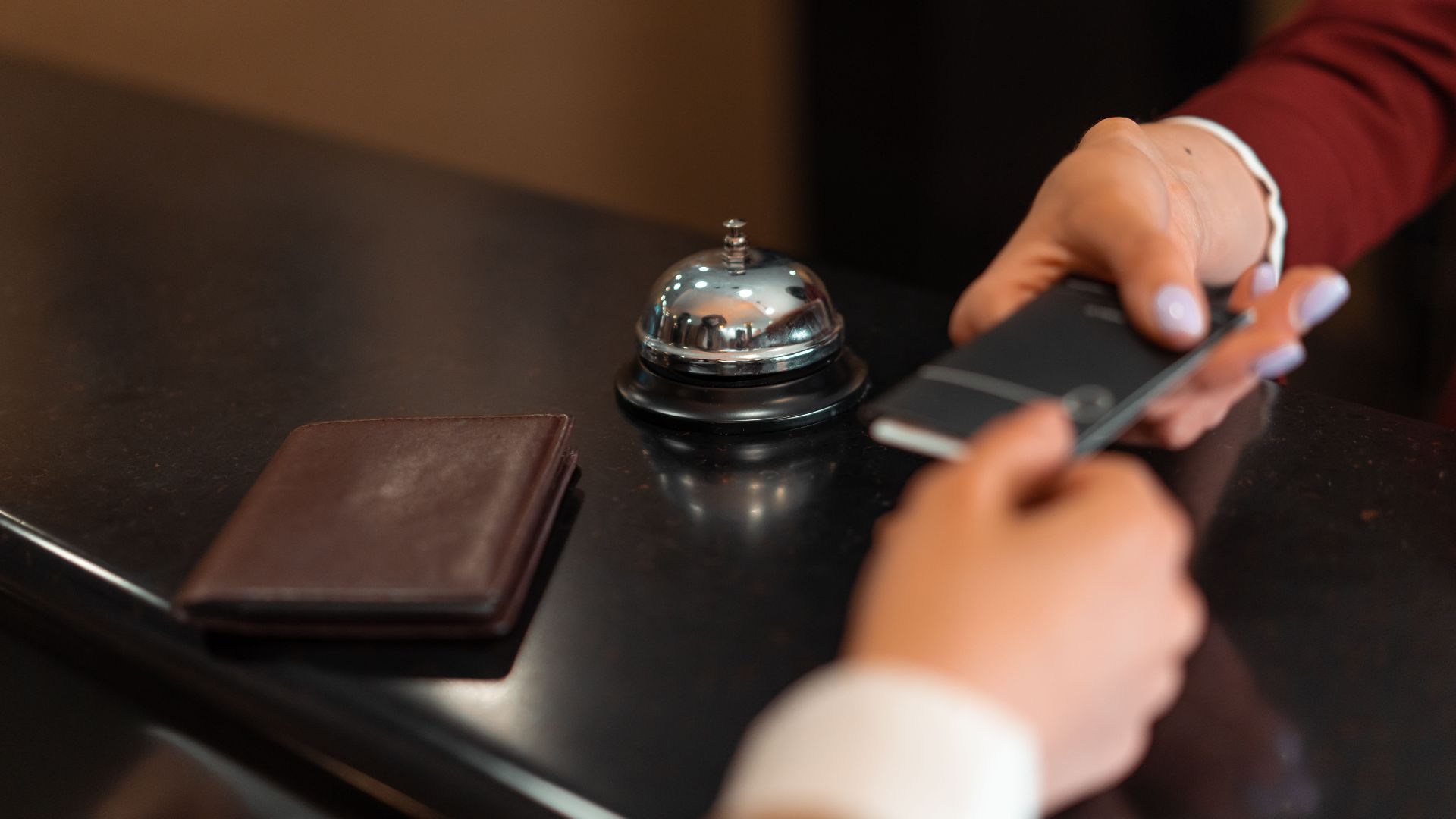 A close-up of a hotel check-in process with a smartphone and card transaction at the reception desk.