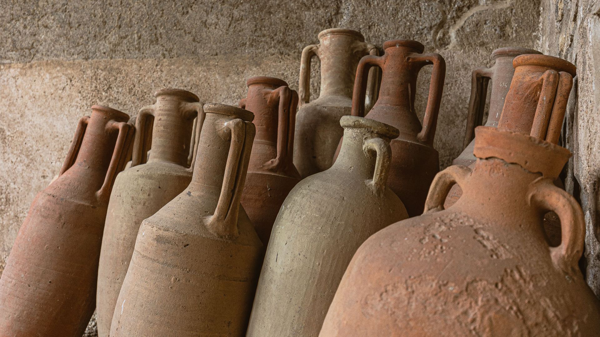 Rustic clay jars arranged against a textured stone wall, showcasing ancient craftsmanship.