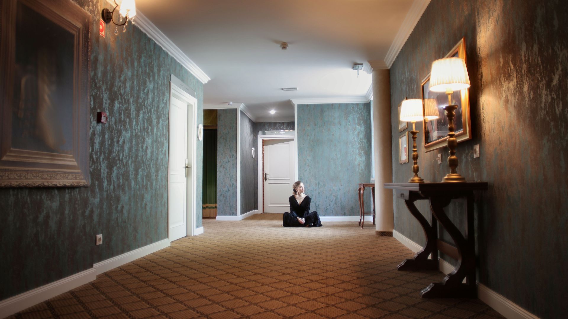 A woman sits peacefully in a luxurious hallway with elegant lamps and decor.