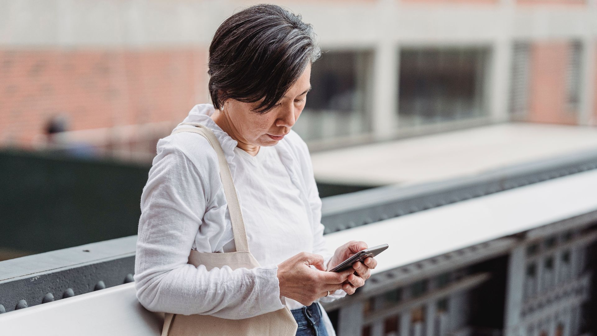 Casual scene of a woman interacting with her smartphone outdoors, leaning on railings.